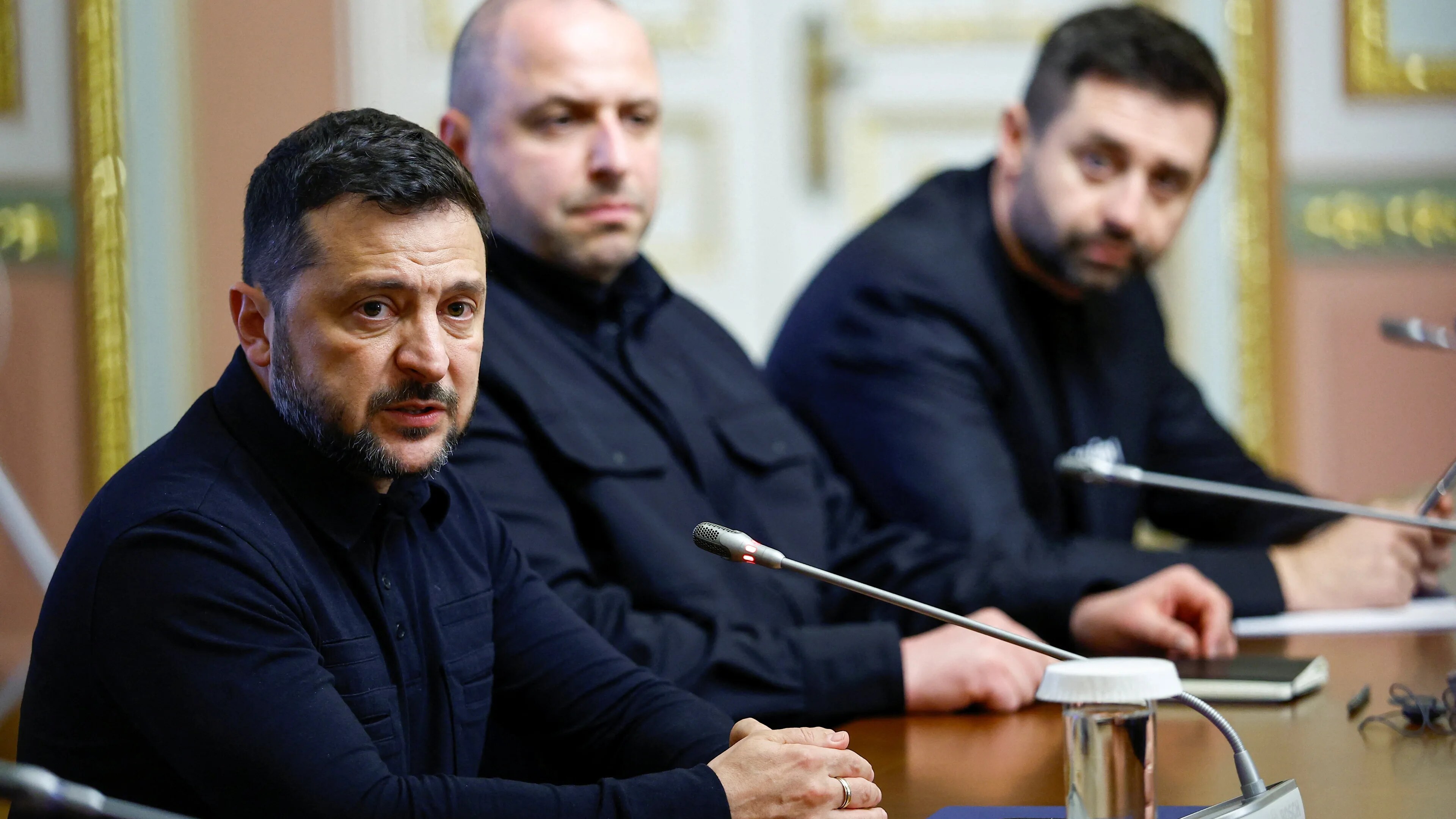 Volodymyr Zelenskyj sitter ved et bord med to menn i et møterom. (Bildebeskrivelsen er laget av en KI-tjeneste)