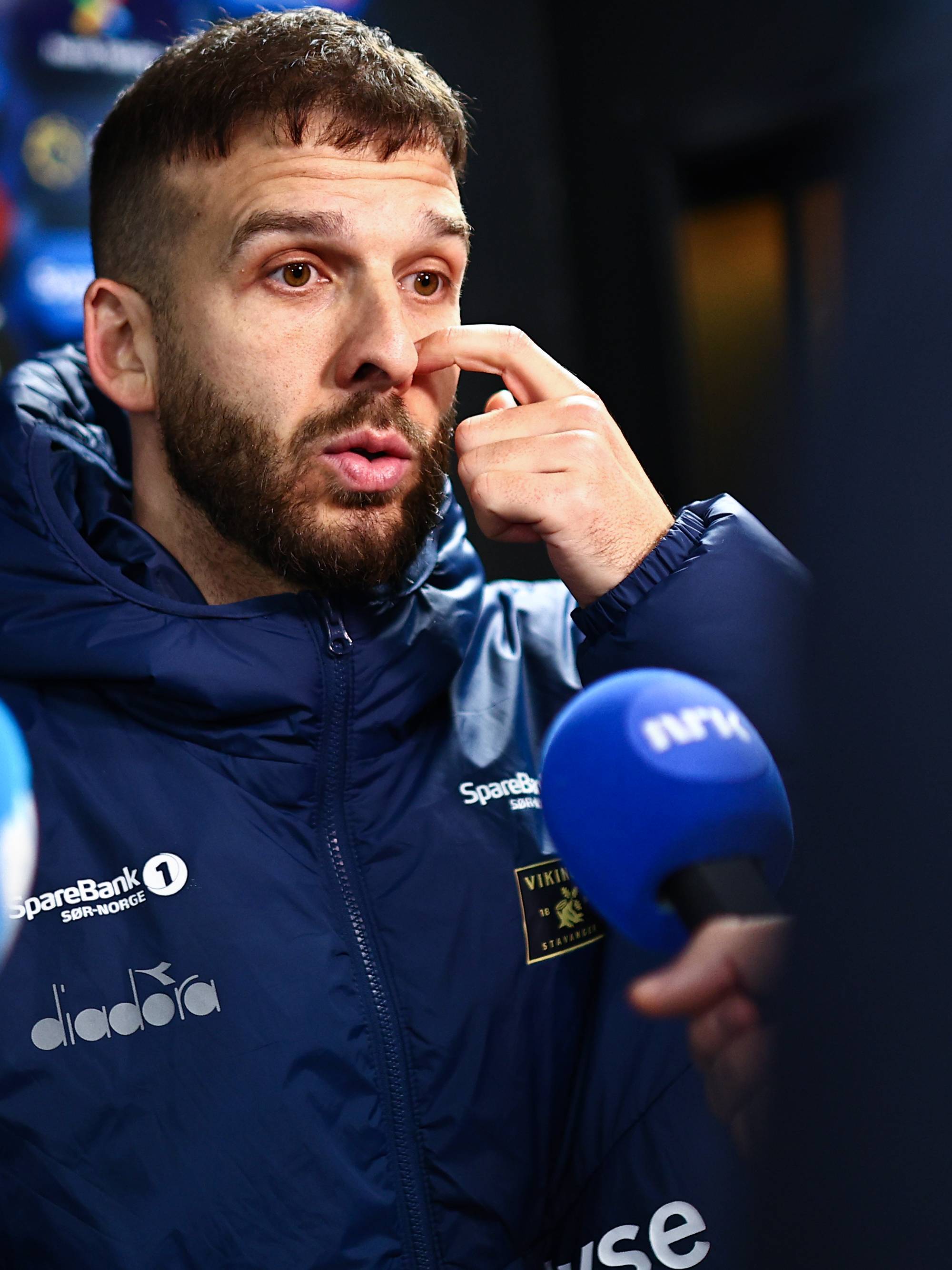 Fotballtrener intervjues av journalister foran en reklamevegg etter kamp. (Bildebeskrivelsen er laget av en KI-tjeneste)