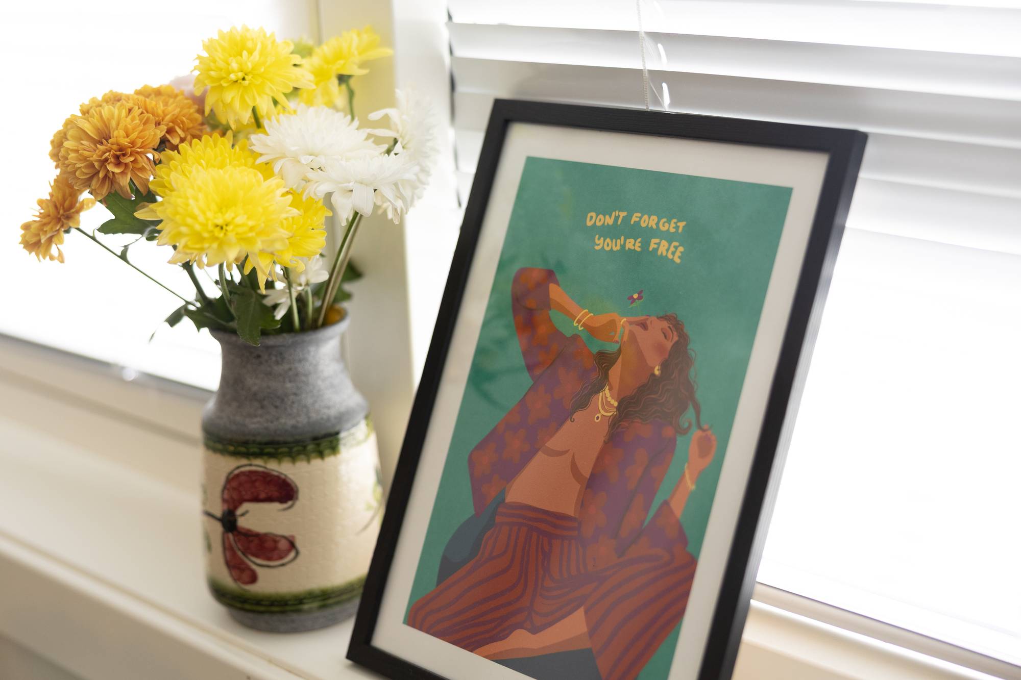 Illustrasjon i ramme med teksten «Don't forget you're free» ved siden av en vase med blomster. 
