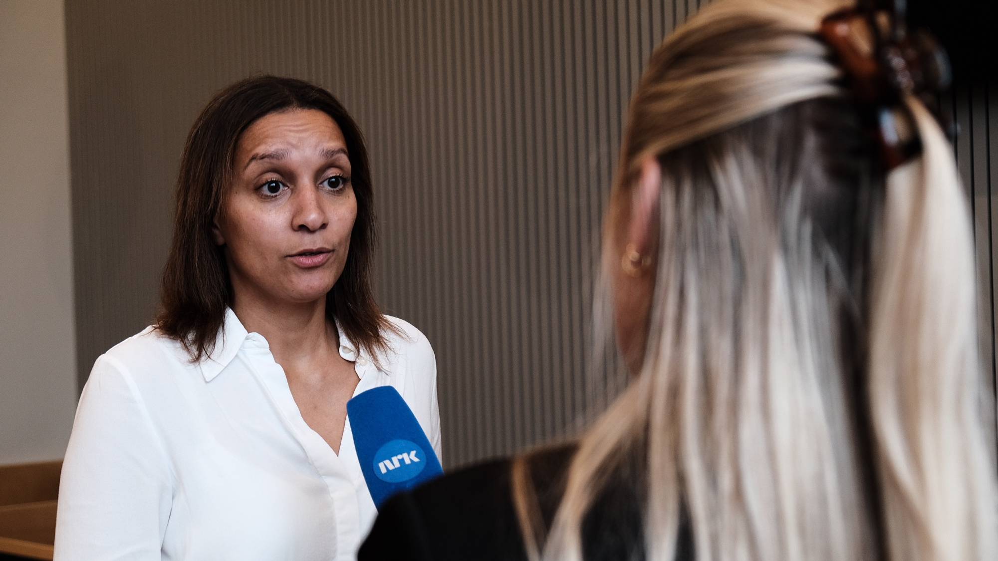 En kvinne blir intervjuet av en journalist med en NRK-mikrofon. (Bildebeskrivelsen er laget av en KI-tjeneste)