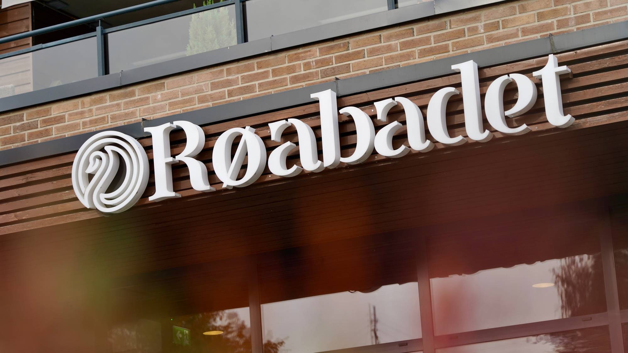 Skilt med teksten Røabadet i hvite bokstaver på en murvegg over en inngang. (Bildebeskrivelsen er laget av en KI-tjeneste)