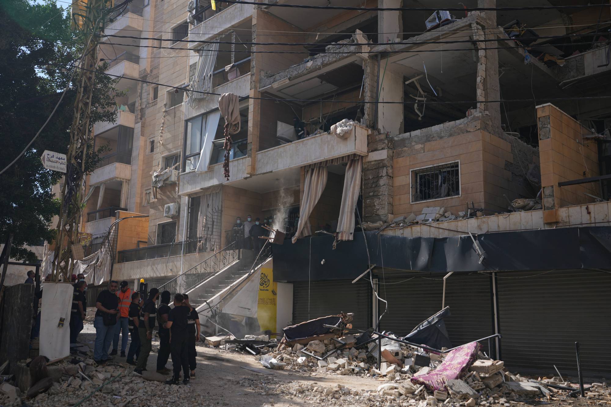 En bygning i Beirut er betydelig skadet, trolig etter en eksplosjon. Flere personer, noen i uniform, står utenfor og ser på ruinene. Mye bygningsrester ligger strødd i gaten.