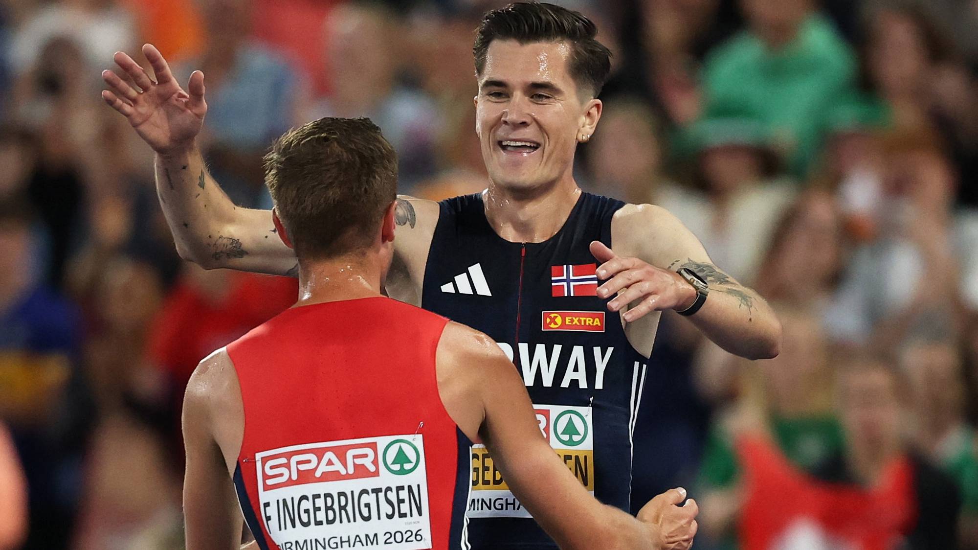 Filip Ingebrigtsen omfavner en annen utøver i norsk landslagsdrakt etter et løp. (Bildebeskrivelsen er laget av en KI-tjeneste)