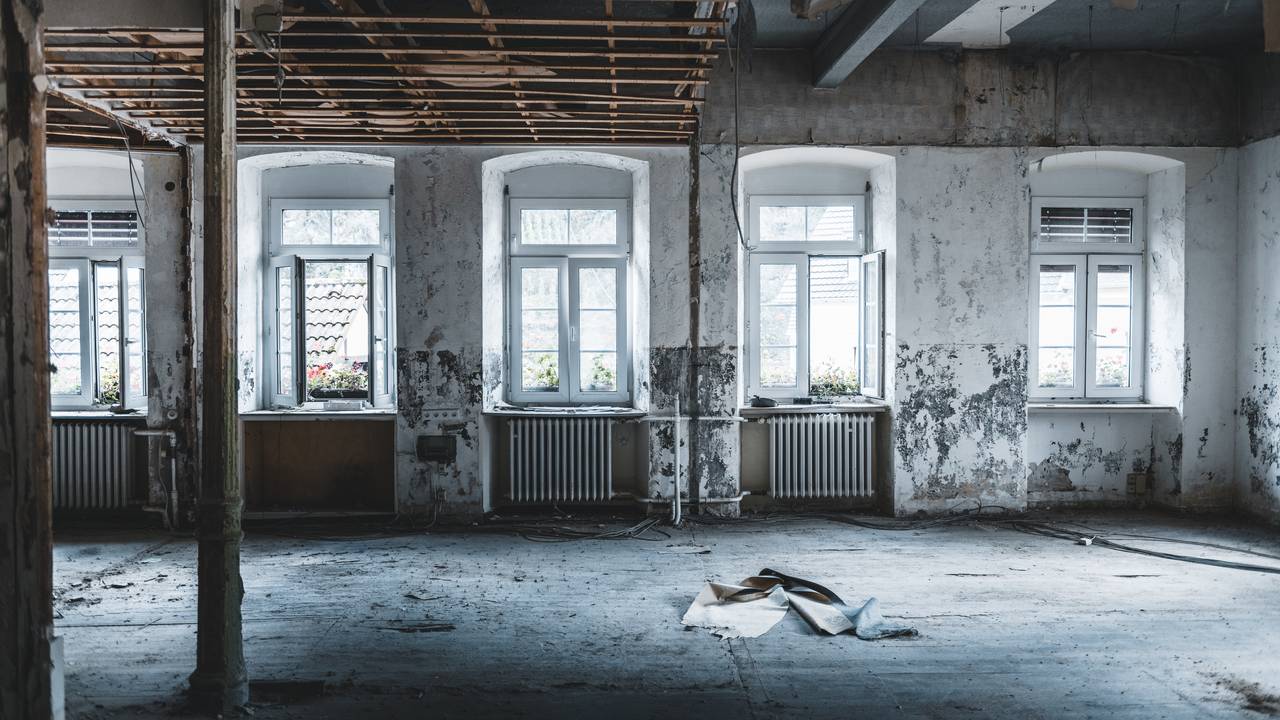 Innsiden av et hus som har blitt ødelagt av flom. Vinduer i bakgrunnen og rester av papir i forgrunnen.