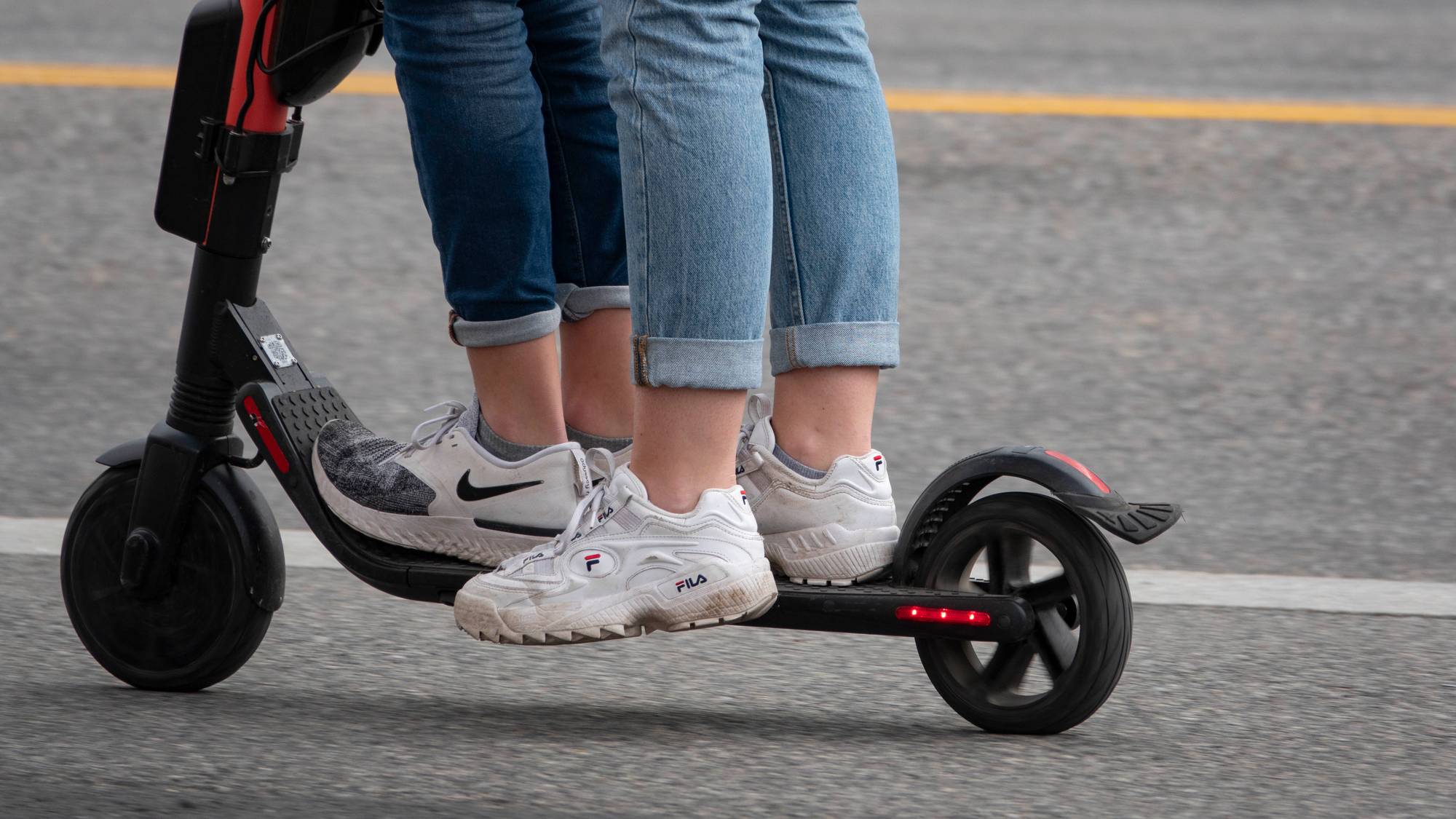 Vi ser beina til to personer som står på samme elsparkesykkel