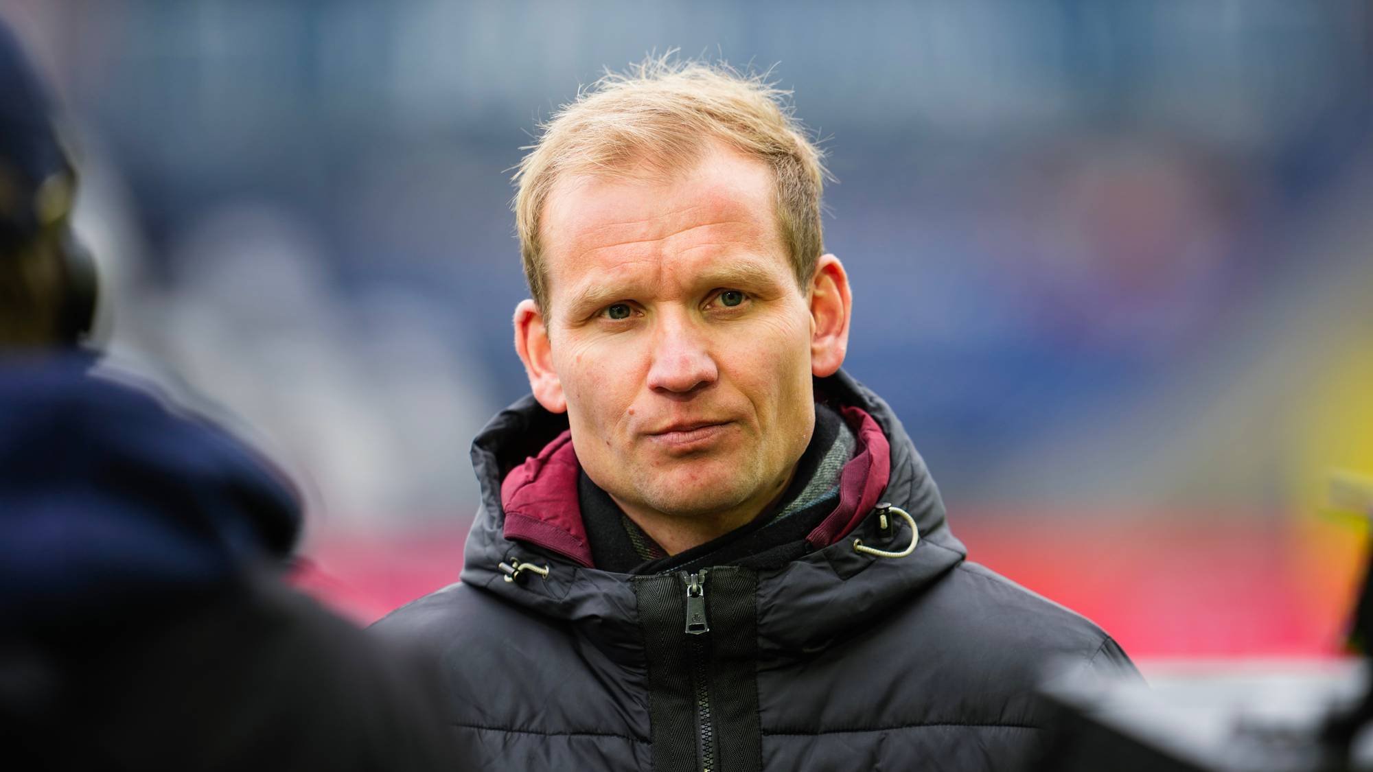 Portrett av fotballtrener Kjetil Knutsen i en mørk jakke på en fotballstadion. (Bildebeskrivelsen er laget av en KI-tjeneste)