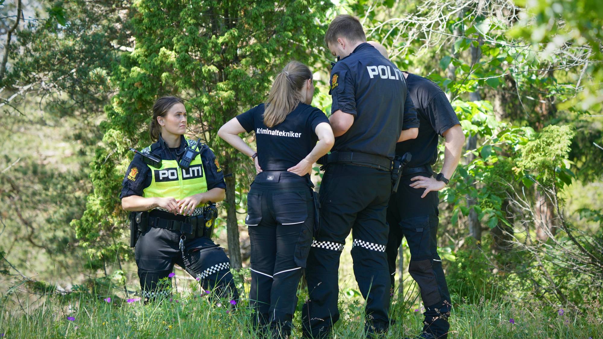 Flere uniformerte politifolk står i en skog.