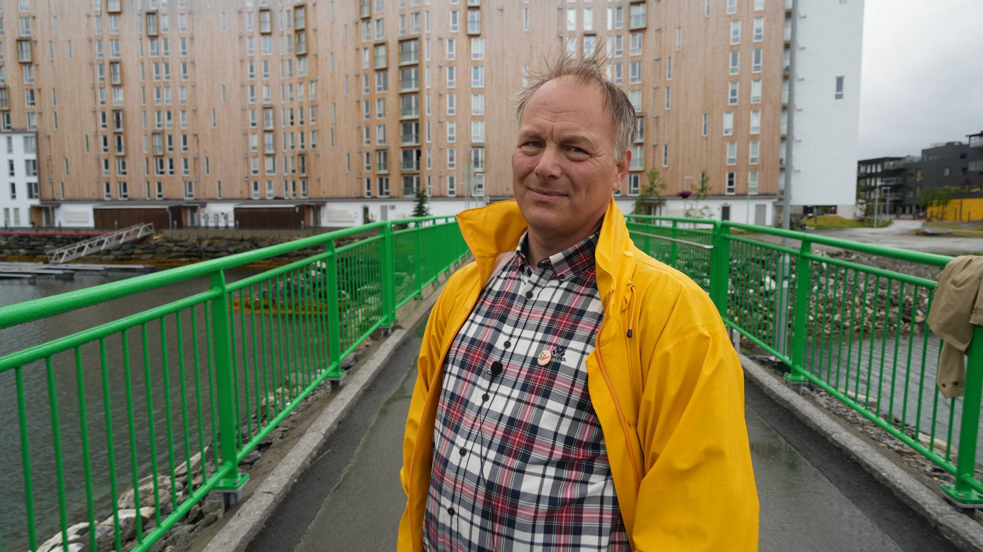Mann i gul jakke med bygning i bakgrunnen