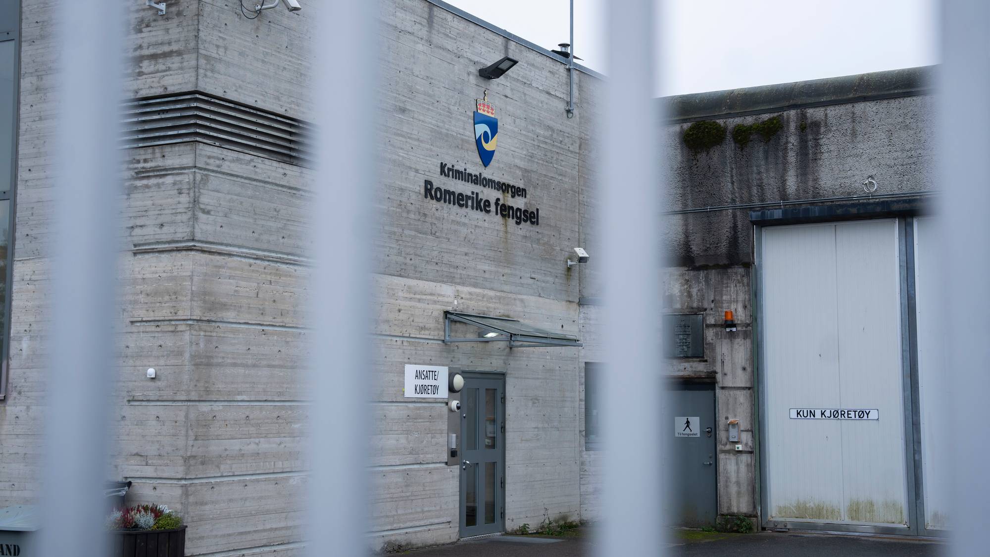 Fasaden til Romerike fengsel sett gjennom et gjerde. Inngangspartier og skilt er synlige. (Bildebeskrivelsen er laget av en KI-tjeneste)