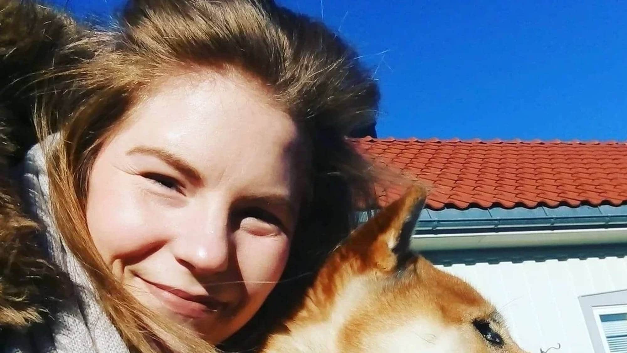 En kvinne og en hund foran et hus.