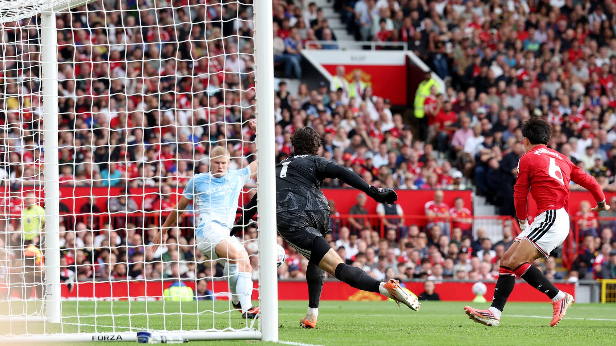 Erling Haaland skyter mot mål i en fotballkamp mot Manchester United foran fullsatte tribuner. (Bildebeskrivelsen er laget av en KI-tjeneste)