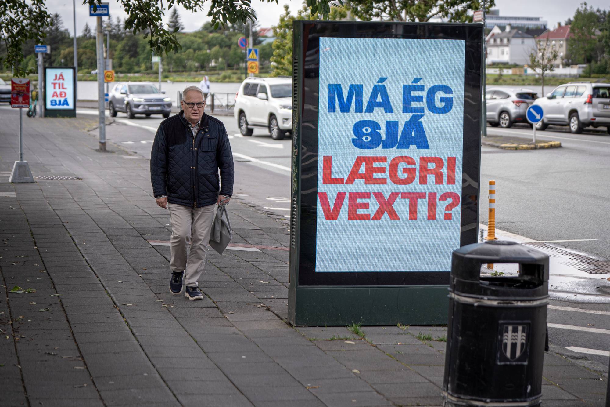 Eldre mann går på fortauet ved stor plakat på Island