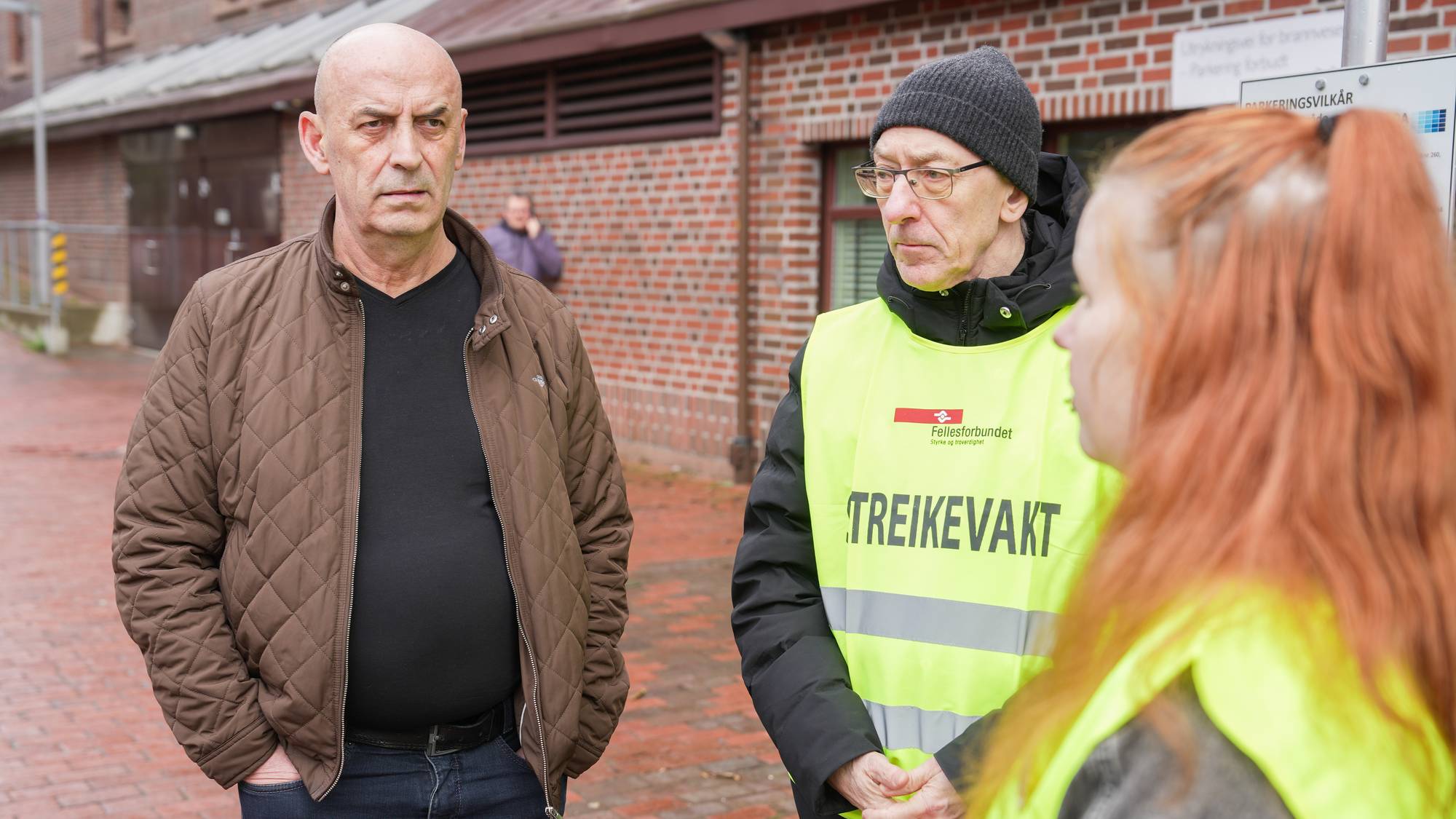 en mann som ser streng ut snakker med to personer i refleksvest