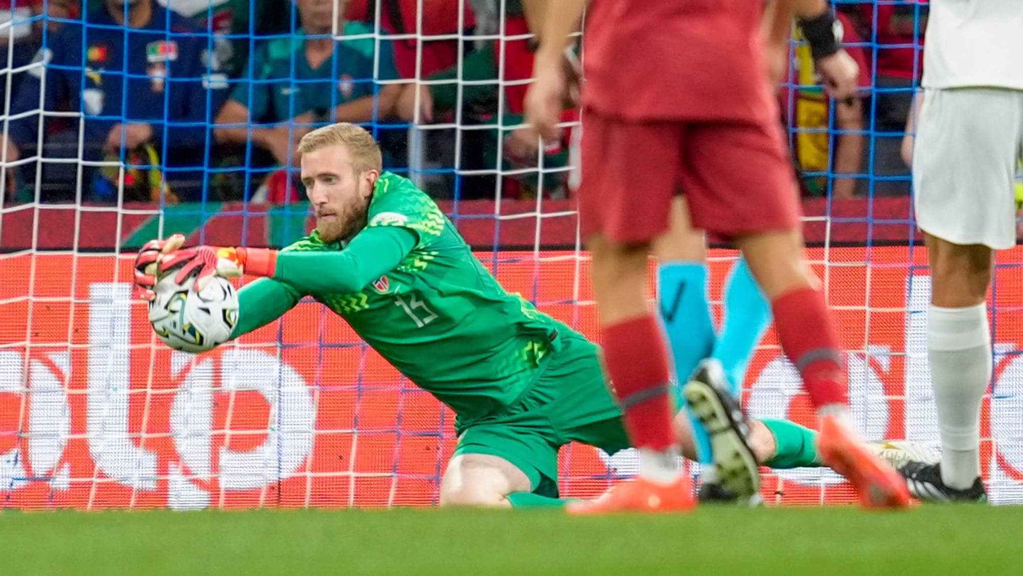 Fotballkeeper i grønn drakt redder en ball foran målet på en stadion. (Bildebeskrivelsen er laget av en KI-tjeneste)