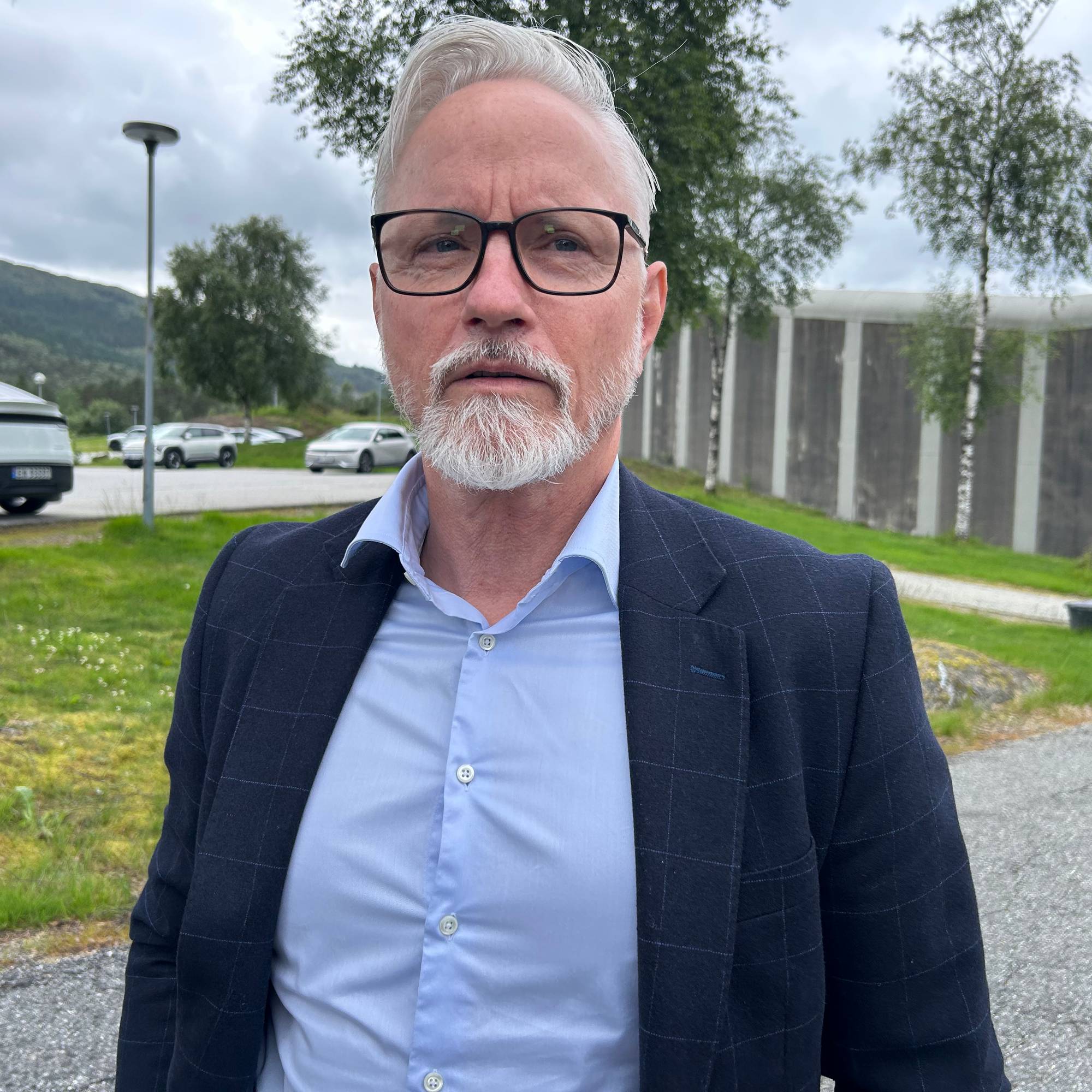 En mann med briller i dressjakke foran en fengselsmur.