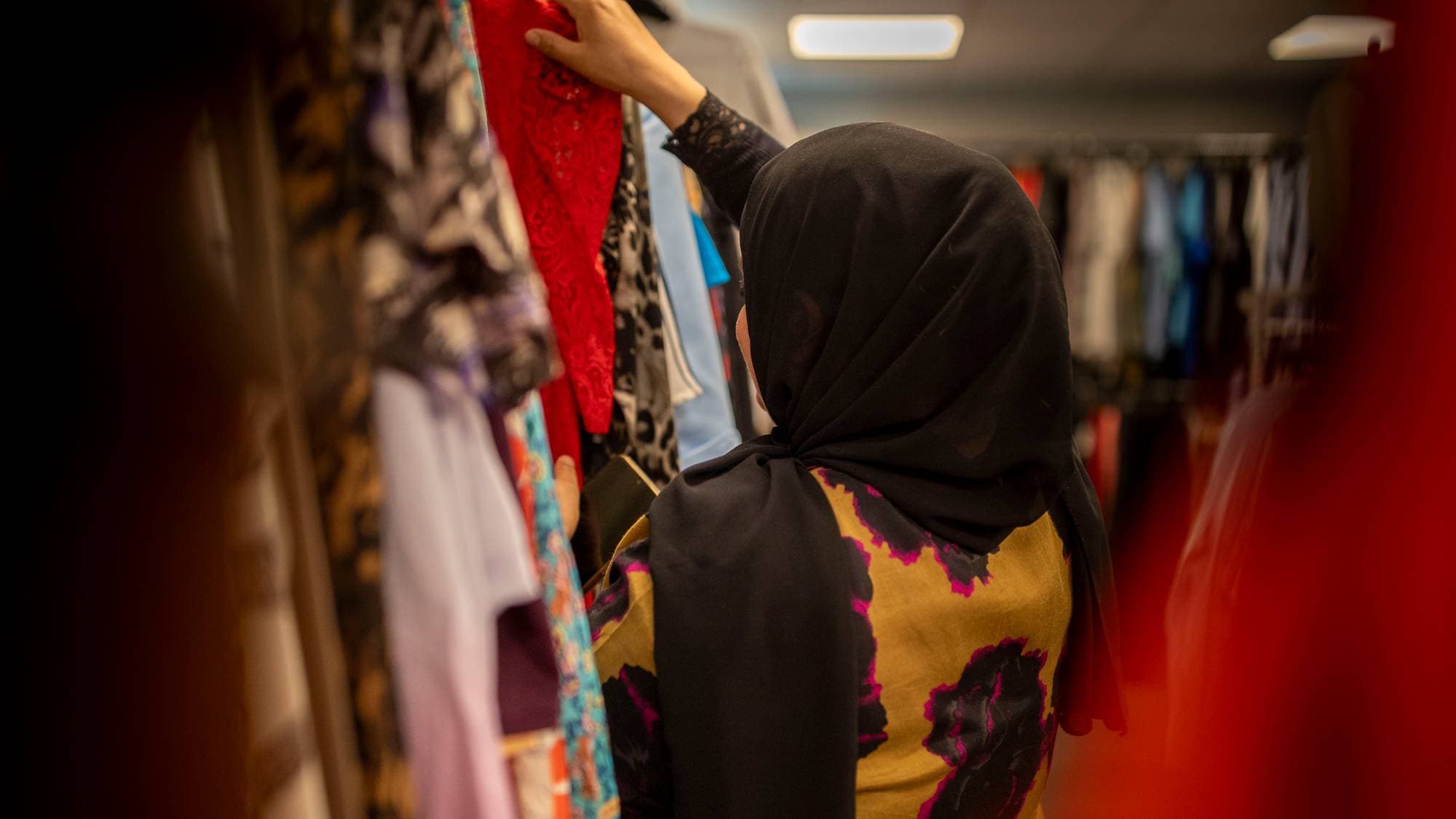 Maria bakfra inne i bruktbutikken der hun jobber. Hun har på seg hijab og kjole