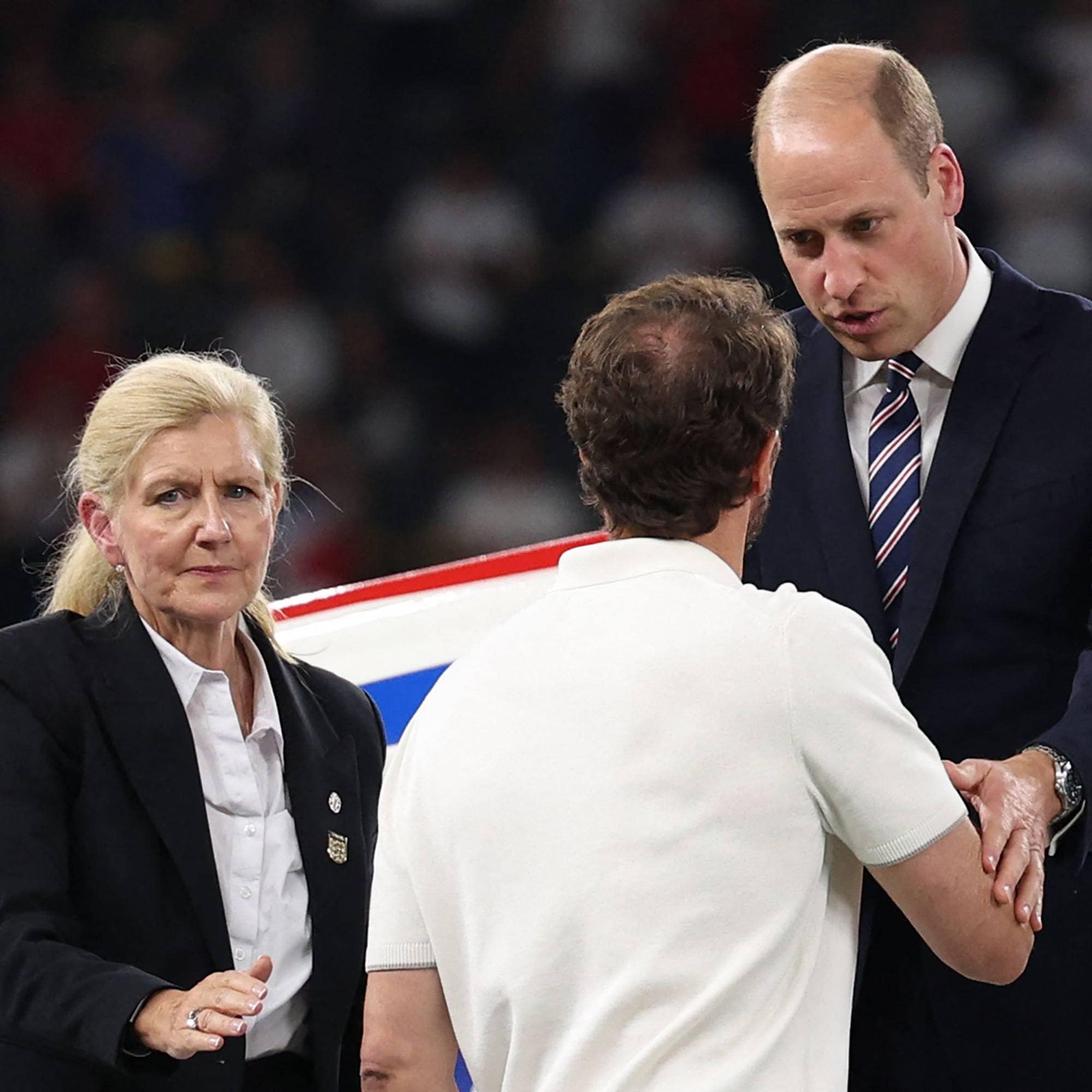 Prins William hilser på en mann, mens en kvinne i dress står ved siden av på en sportsarena. (Bildebeskrivelsen er laget av en KI-tjeneste)