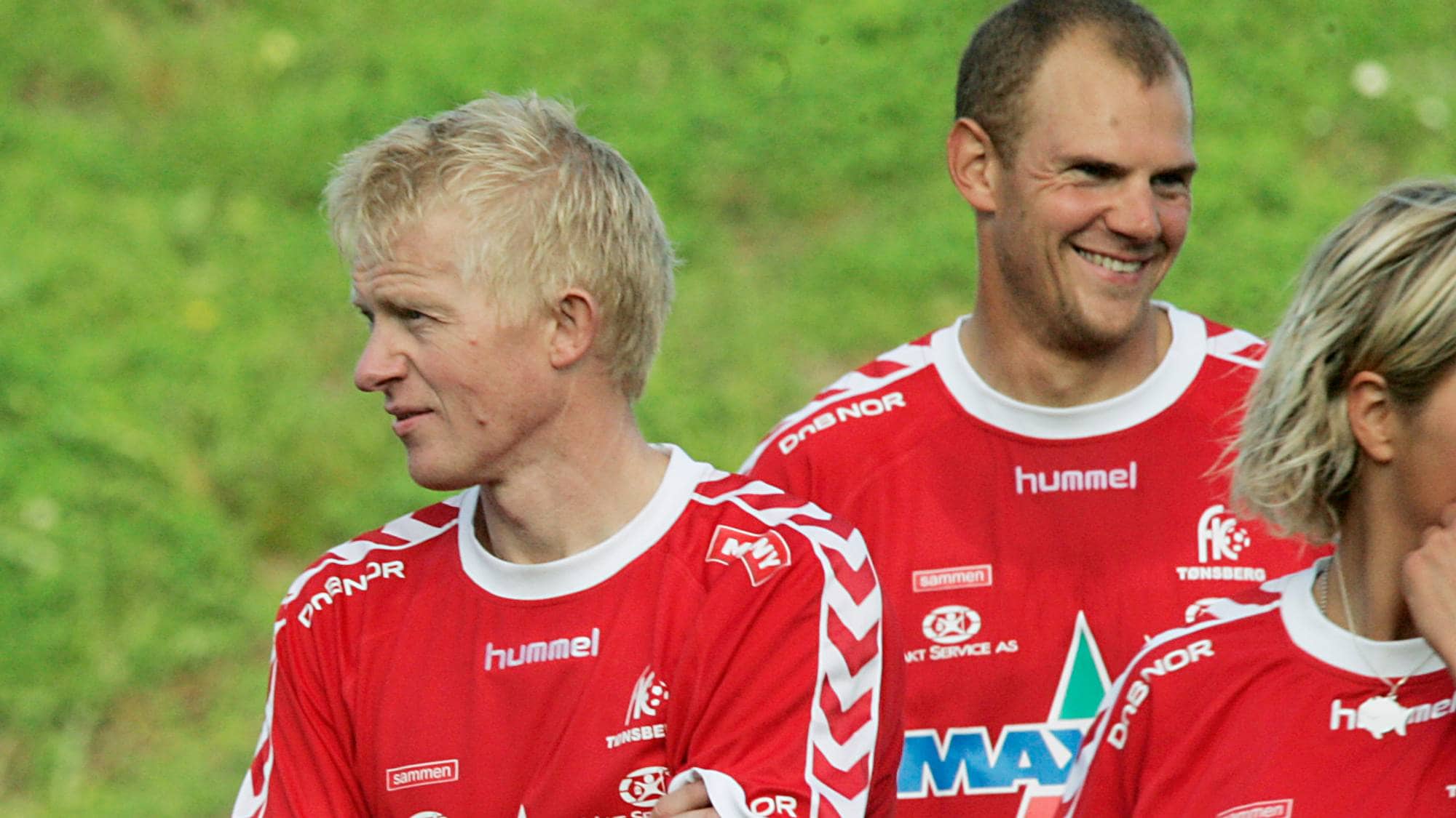 Trenere og fotballspillere i røde drakter står på en gressbane. (Bildebeskrivelsen er laget av en KI-tjeneste)