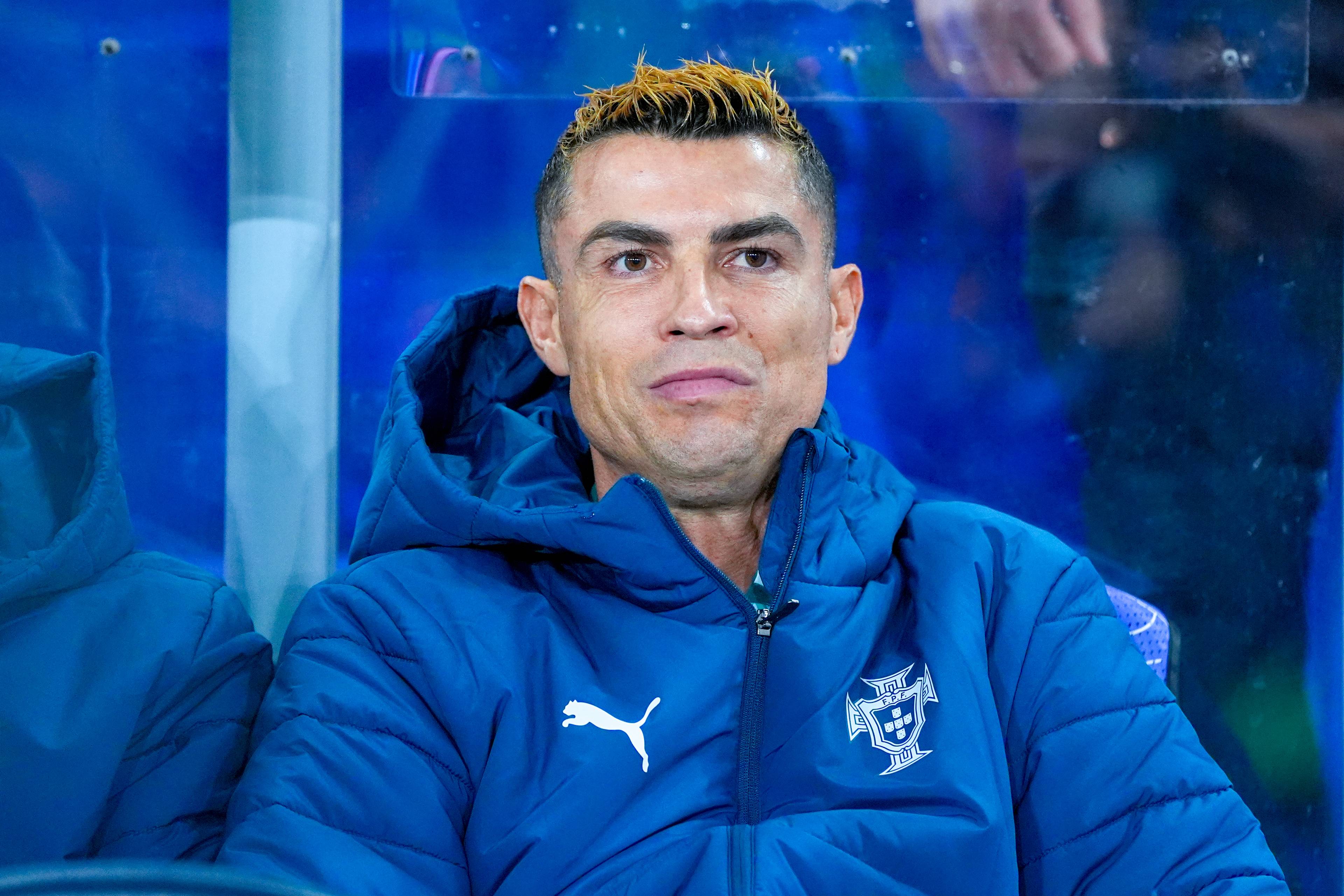 Cristiano Ronaldo sitter på benken iført en blå jakke med det portugisiske fotballforbundets logo. (Bildebeskrivelsen er laget av en KI-tjeneste)