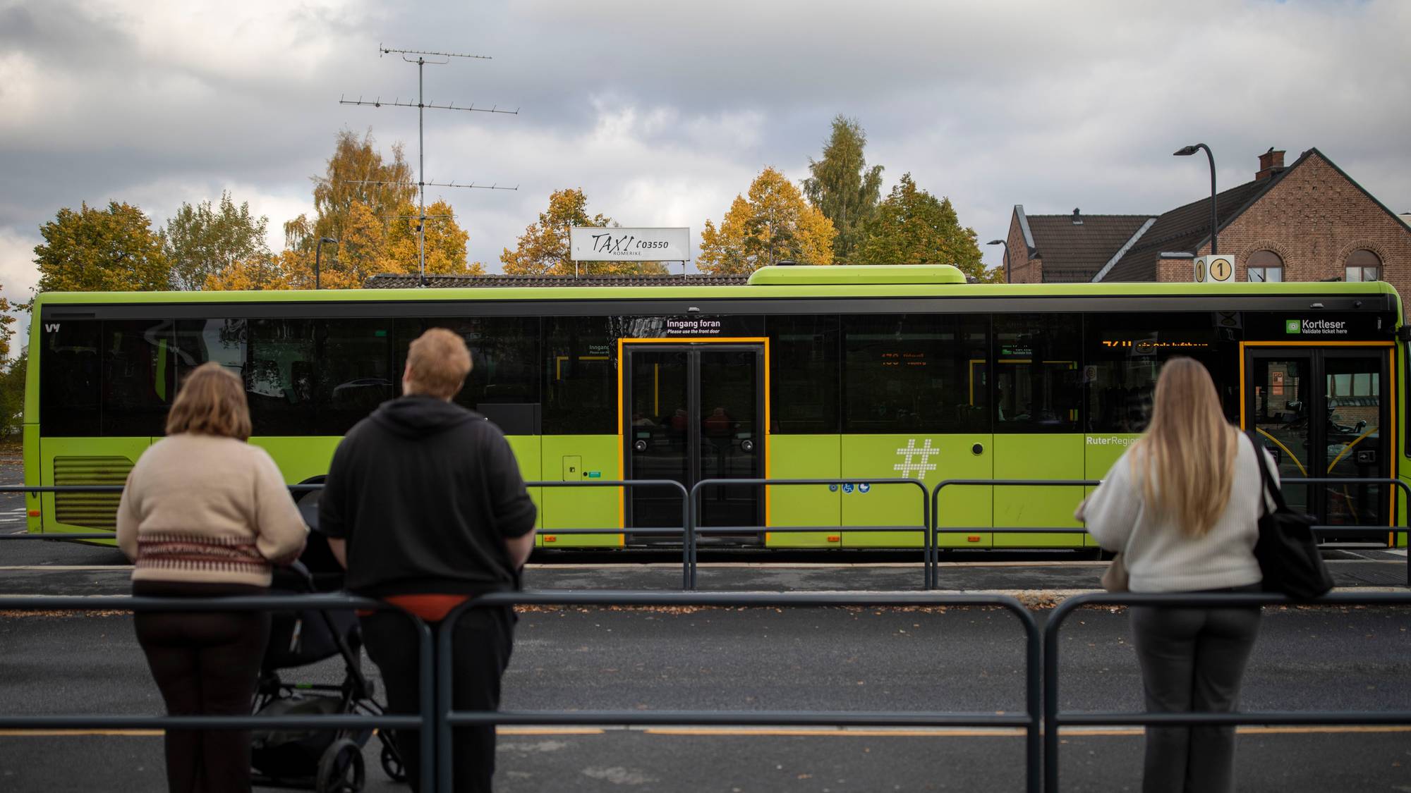 Folk lent til gjerde ser på grønn buss
