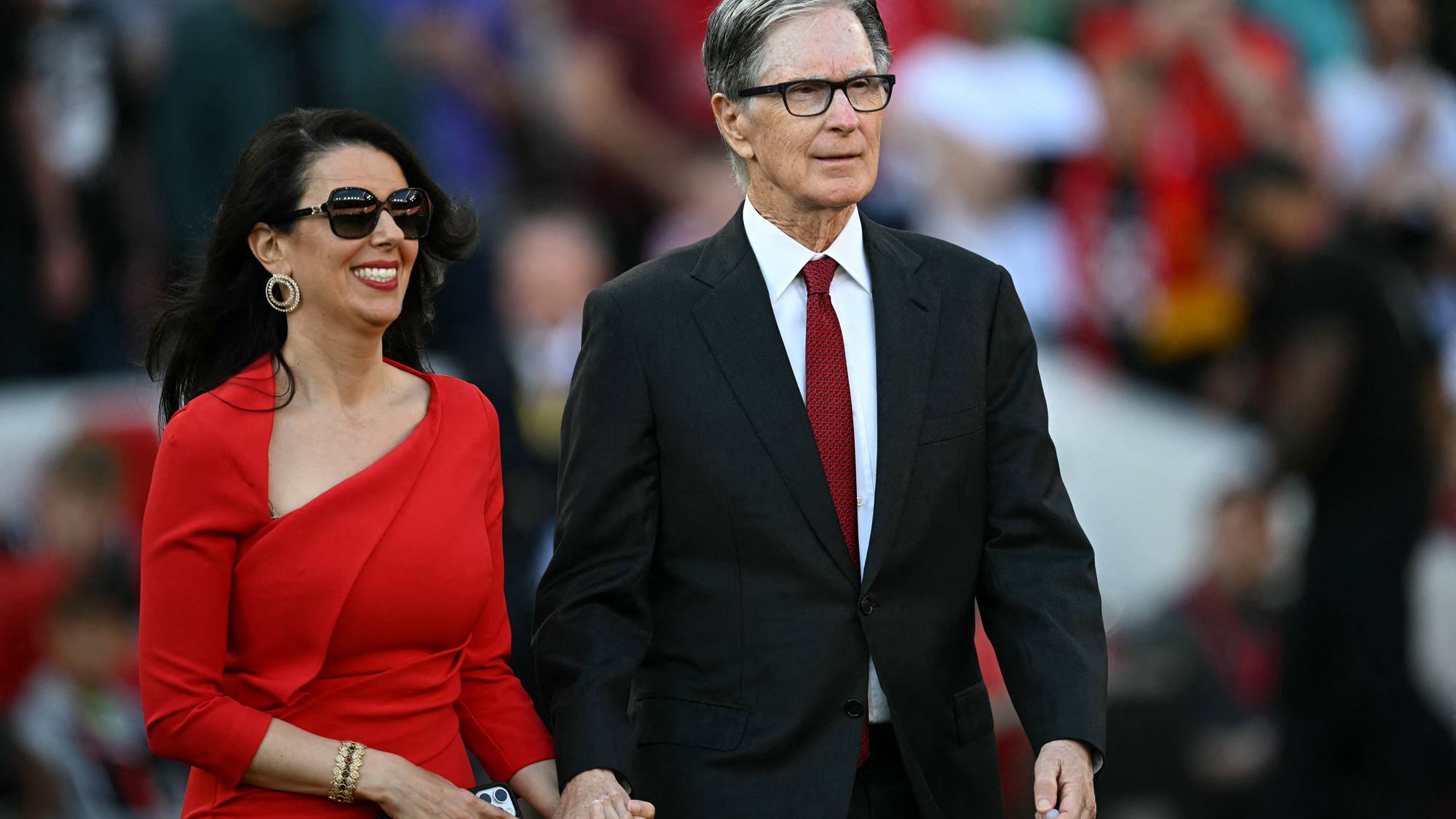 Linda Pizzuti og John W. Henry går hånd i hånd på en fotballstadion. (Bildebeskrivelsen er laget av en KI-tjeneste)