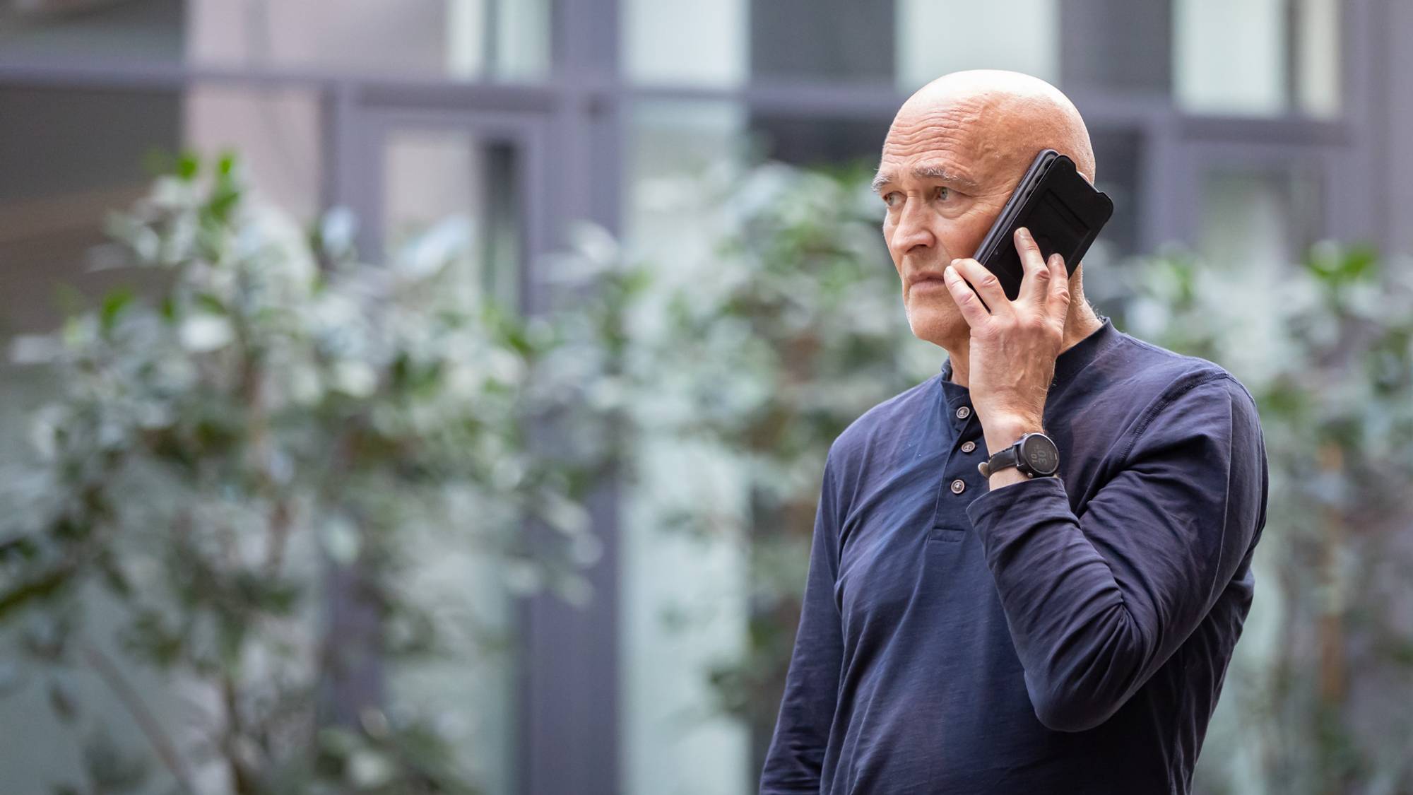 Harry Arne Solberg står og snakker i en mobiltelefon. Han kikker betenkt framover.
