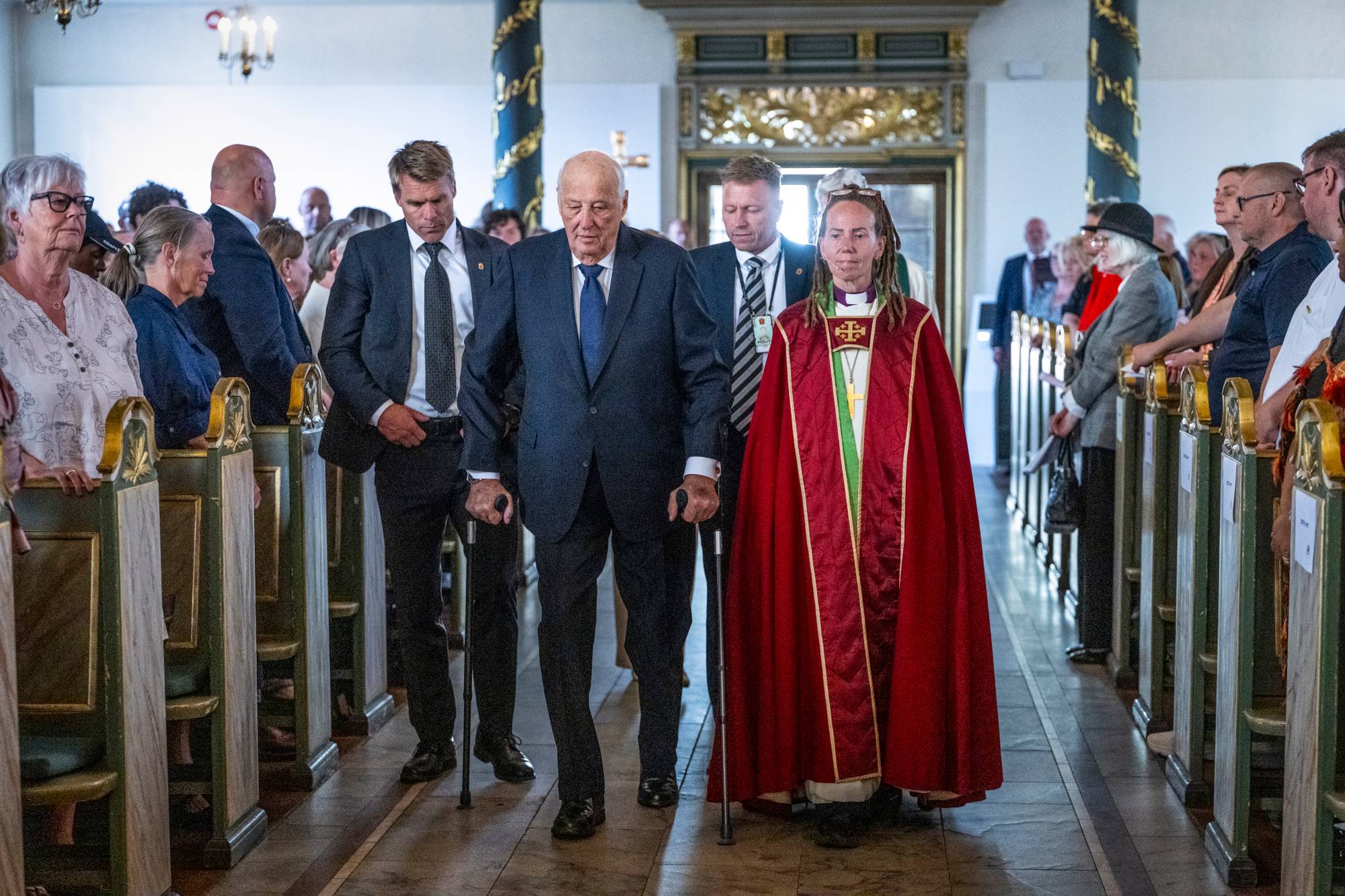 Kong Harald går inn i Oslo domkirke på krykker, ved siden av går Oslo-biskop Sunniva Gylver