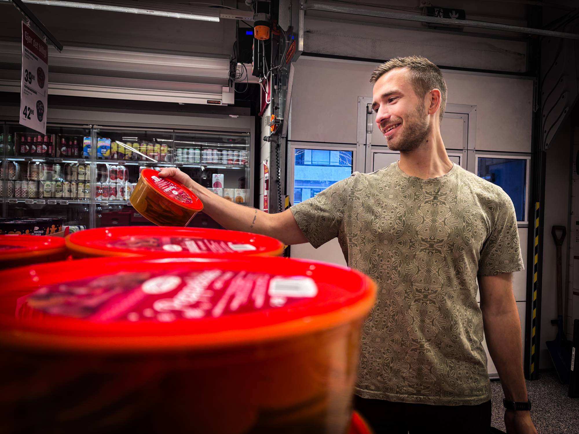 En mann står i en dagligvarebutikk og tar en boks med rød etikett fra en hylle. (Bildebeskrivelsen er laget av en KI-tjeneste)