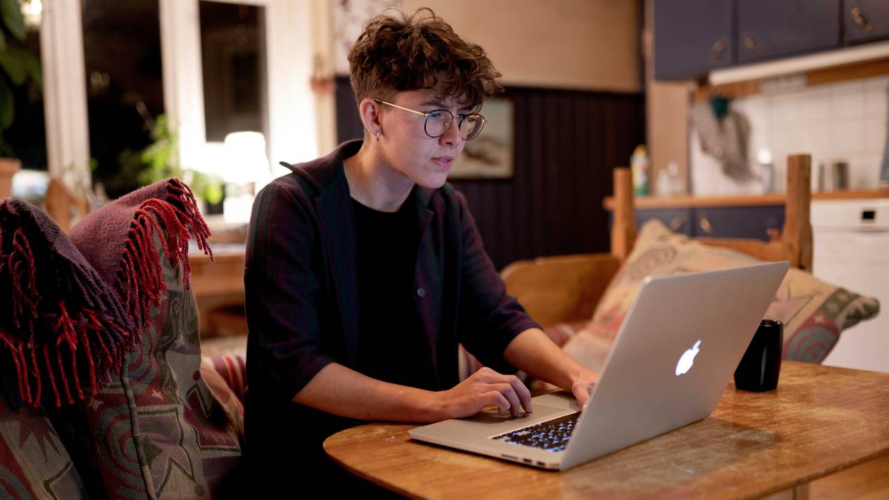 Kvinne foran dataskjerm, sittende på kjøkkenet.