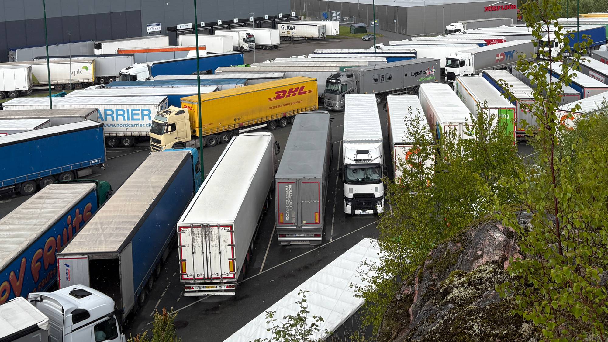 Tett i tett med vogntog fra forskjellige selskap står parkert på en plass i Halden i bakgrunn et stort bygg