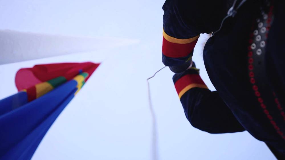 Koftekledd heiser sameflagg i lyst landskap