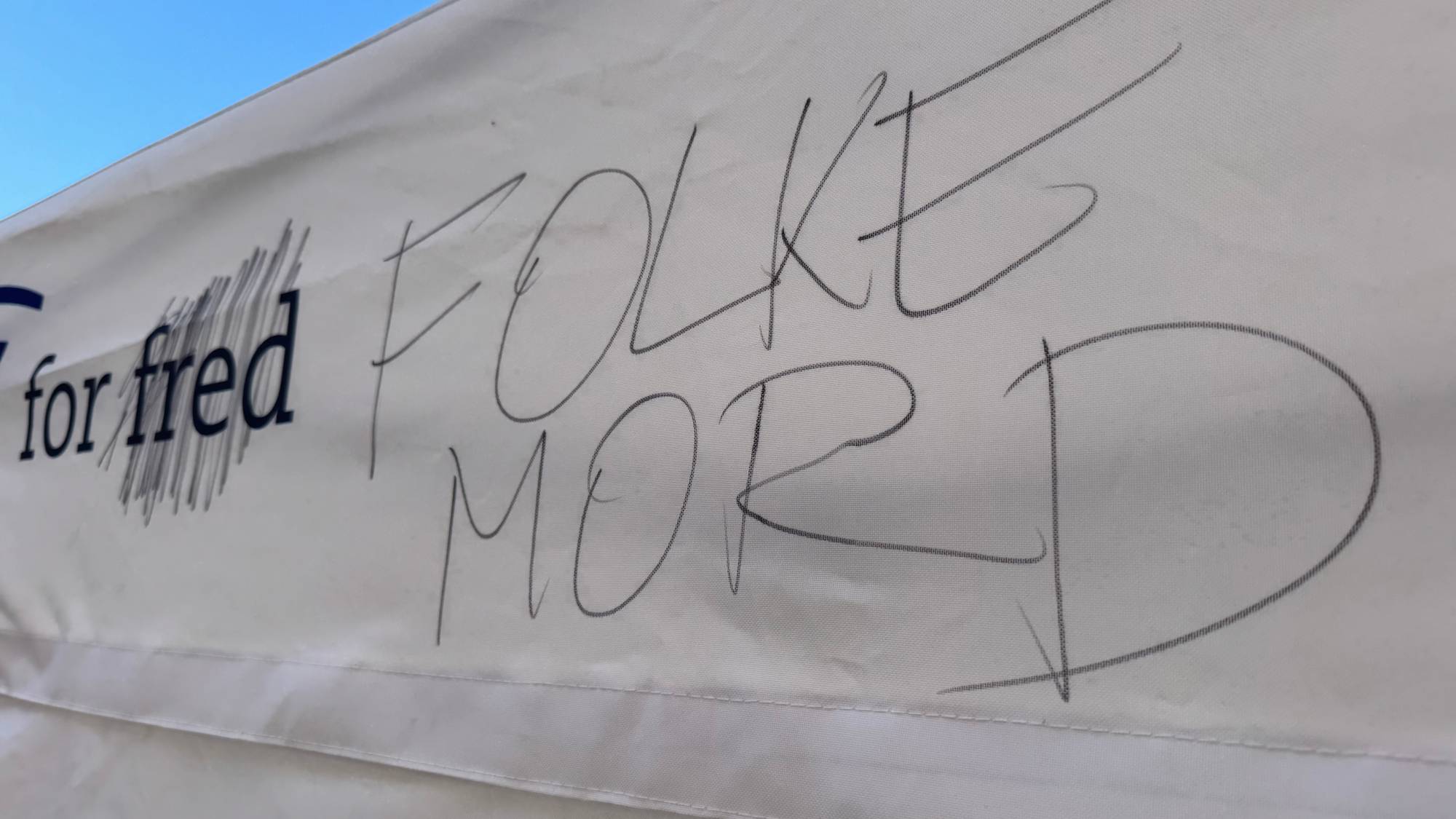 Et hvitt banner med påskriften FOLKEMORD skrevet med svart tusj over ordet fred. (Bildebeskrivelsen er laget av en KI-tjeneste)