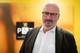 Tom Balgaard / NRK En mann i mørk jakke og hvit skjorte står foran en vegg med logoen til PST. Bakgrunnen er i gult og oransje, og gir kontekst til bildet. Mannen ser alvorlig ut, noe som kan indikere en viktig situasjon. Ingen andre personer er synlige i bildet. (Bildebeskrivelsen er laget av en KI-tjeneste)