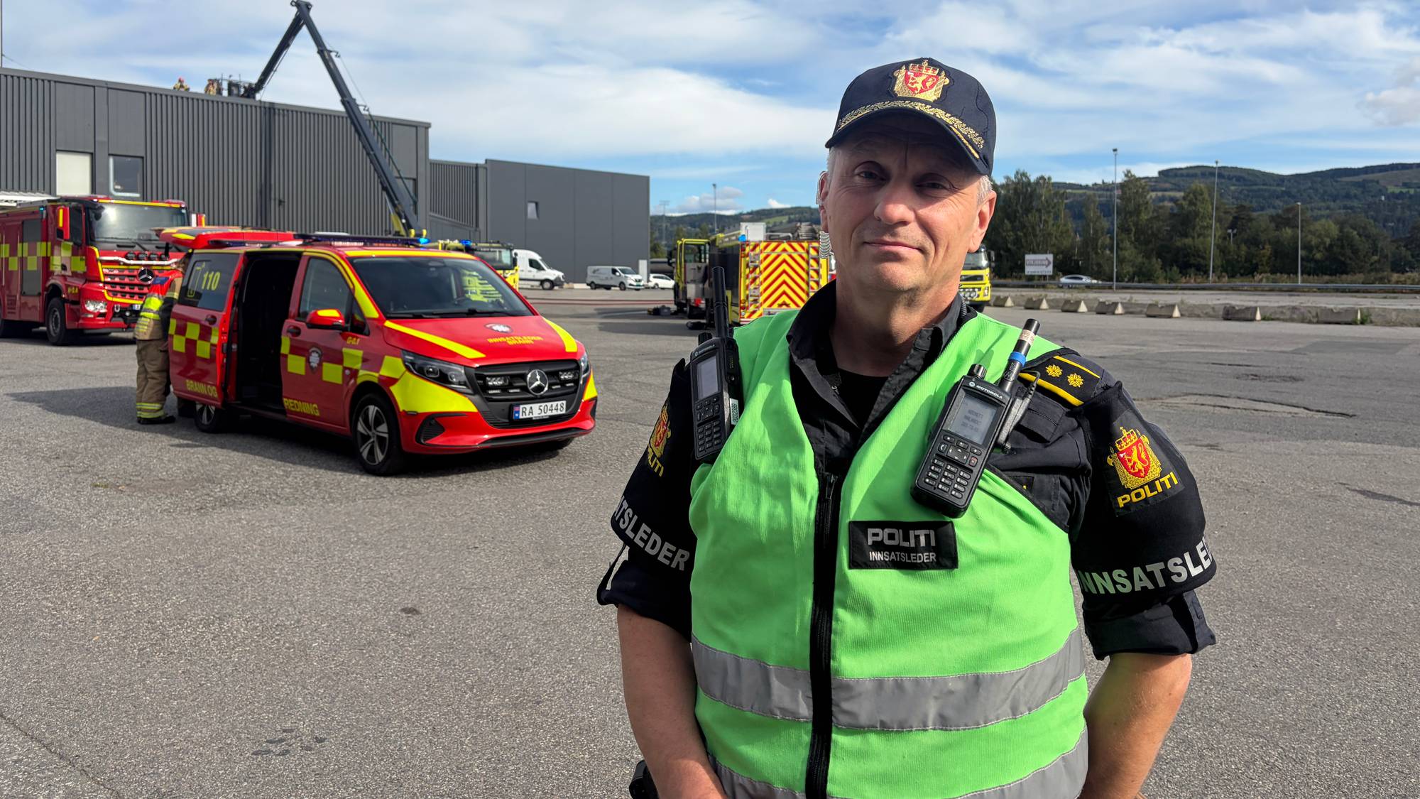 Innsatsleder ved et skadested med brannbiler i bakgrunnen. (Bildebeskrivelsen er laget av en KI-tjeneste)