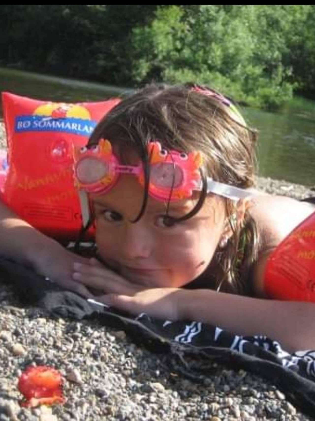 Andrine ligger på stranden med baderinger og svømmebriller.