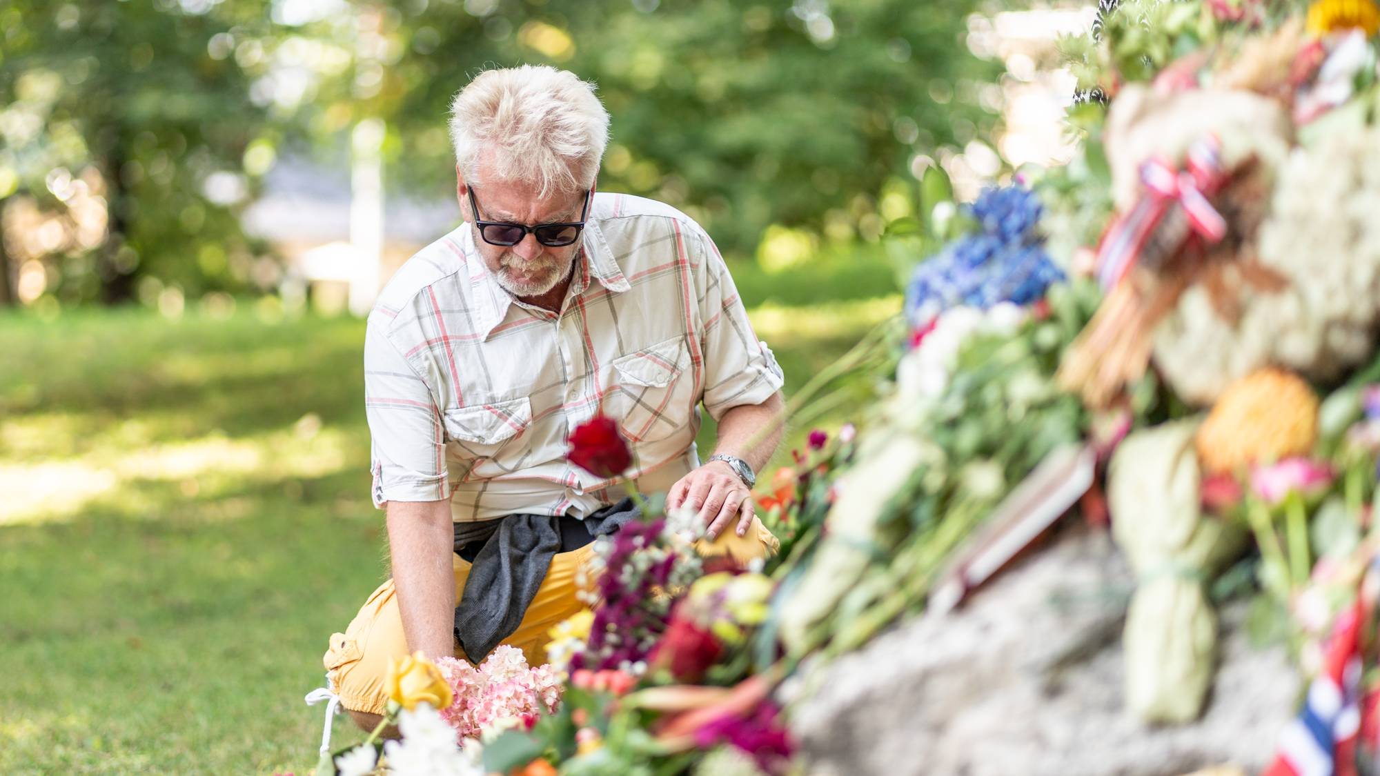 En mann legger ned blomster ved et minnested utendørs. (Bildebeskrivelsen er laget av en KI-tjeneste)