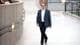 Foto: Erling Slyngstad Hægeland / Privat En mann i dress går forbi en buet betongvegg i en offentlig bygning. I bakgrunnen sitter flere personer på en benk. Gulvflisene er lyse, og det er lamper langs veggen. Omgivelsene tyder på et moderne og urbant miljø. (Bildebeskrivelsen er laget av en KI-tjeneste)