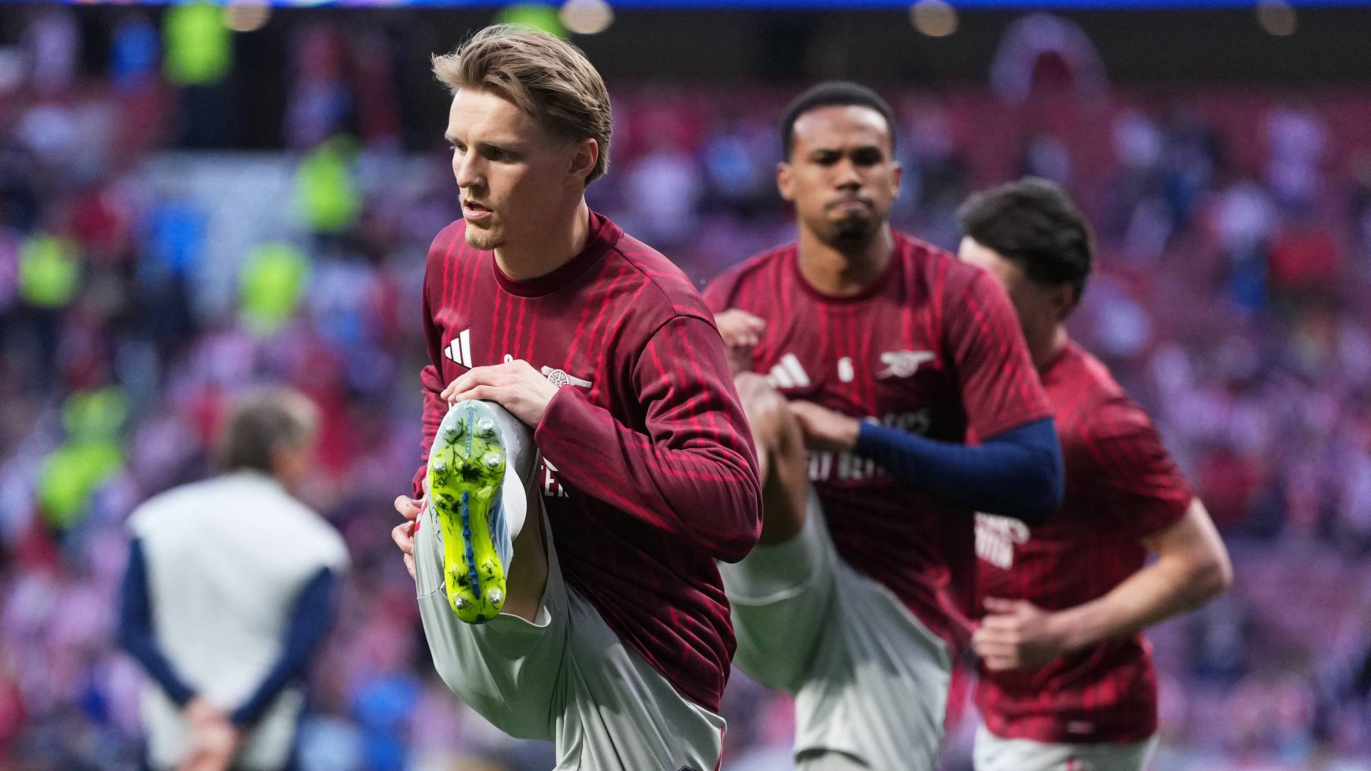 Fotballspillere i oransje drakter tøyer. Én spiller med draktnummer 8 strekker foten med en grønn sko. I bakgrunnen sitter publikum på stadion. (Bildebeskrivelsen er laget av en KI-tjeneste)