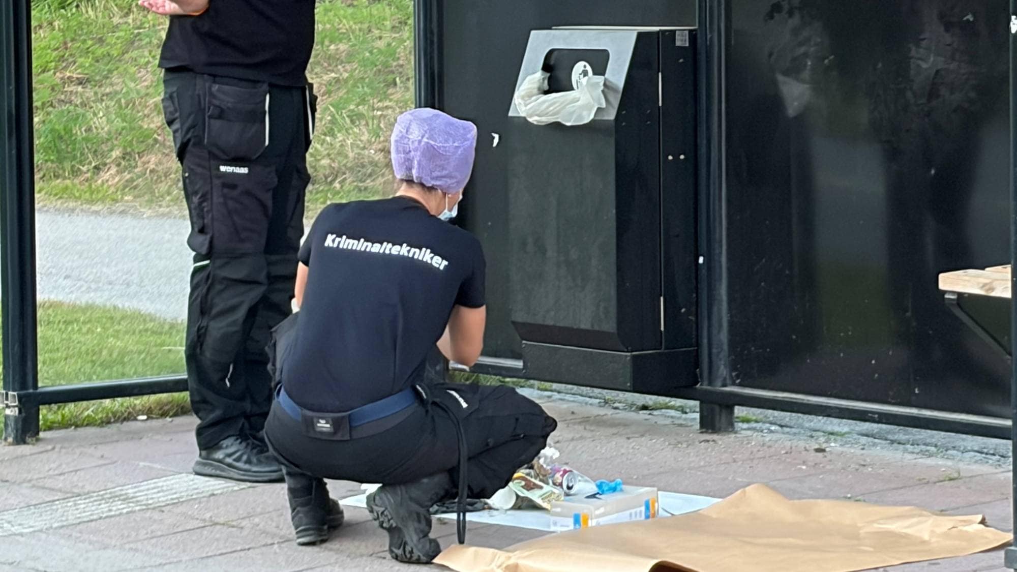 Kriminaltekniker undersøker et busstopp mens en annen person dokumenterer arbeidet med kamera. (Bildebeskrivelsen er laget av en KI-tjeneste)