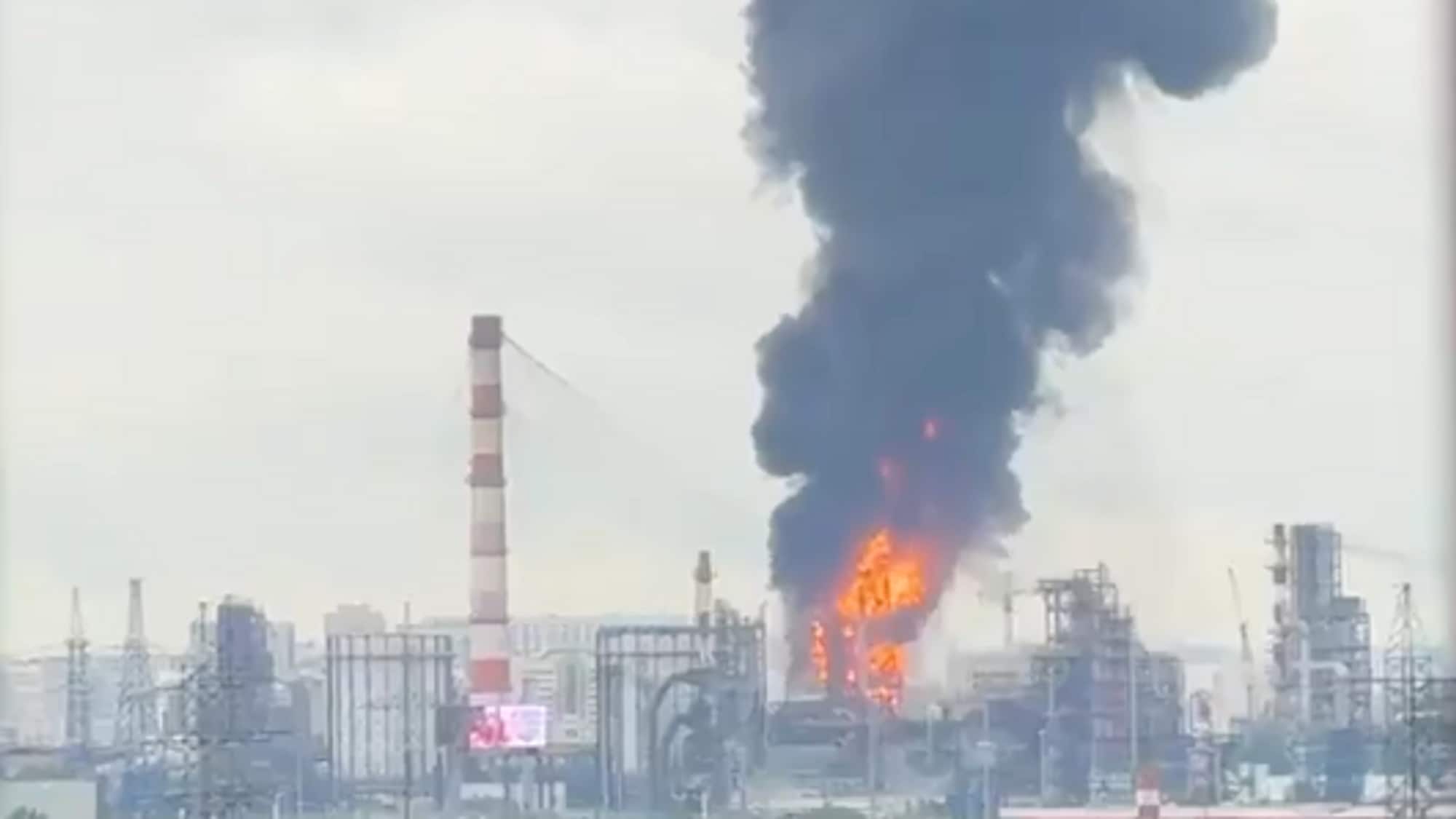 Stor svart røyk stiger fra et industriområde der det brenner i en fabrikk. Flammene er synlige midt i en bygning i anlegget. Andre høye strukturer som piper og tårn er synlige. (Bildebeskrivelsen er laget av en KI-tjeneste)