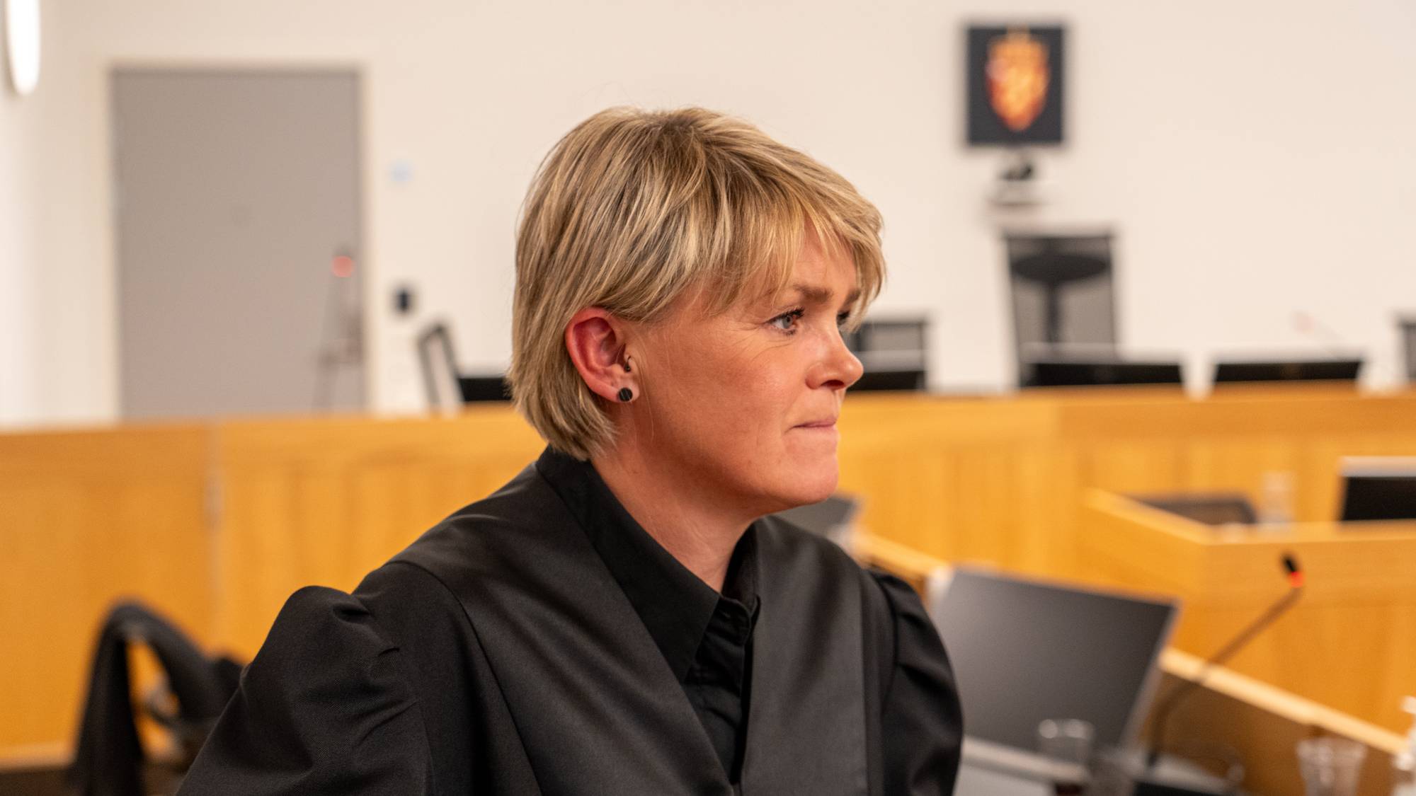 Kvinne med blondt hår iført dommerkappe sitter i en rettssal. (Bildebeskrivelsen er laget av en KI-tjeneste)