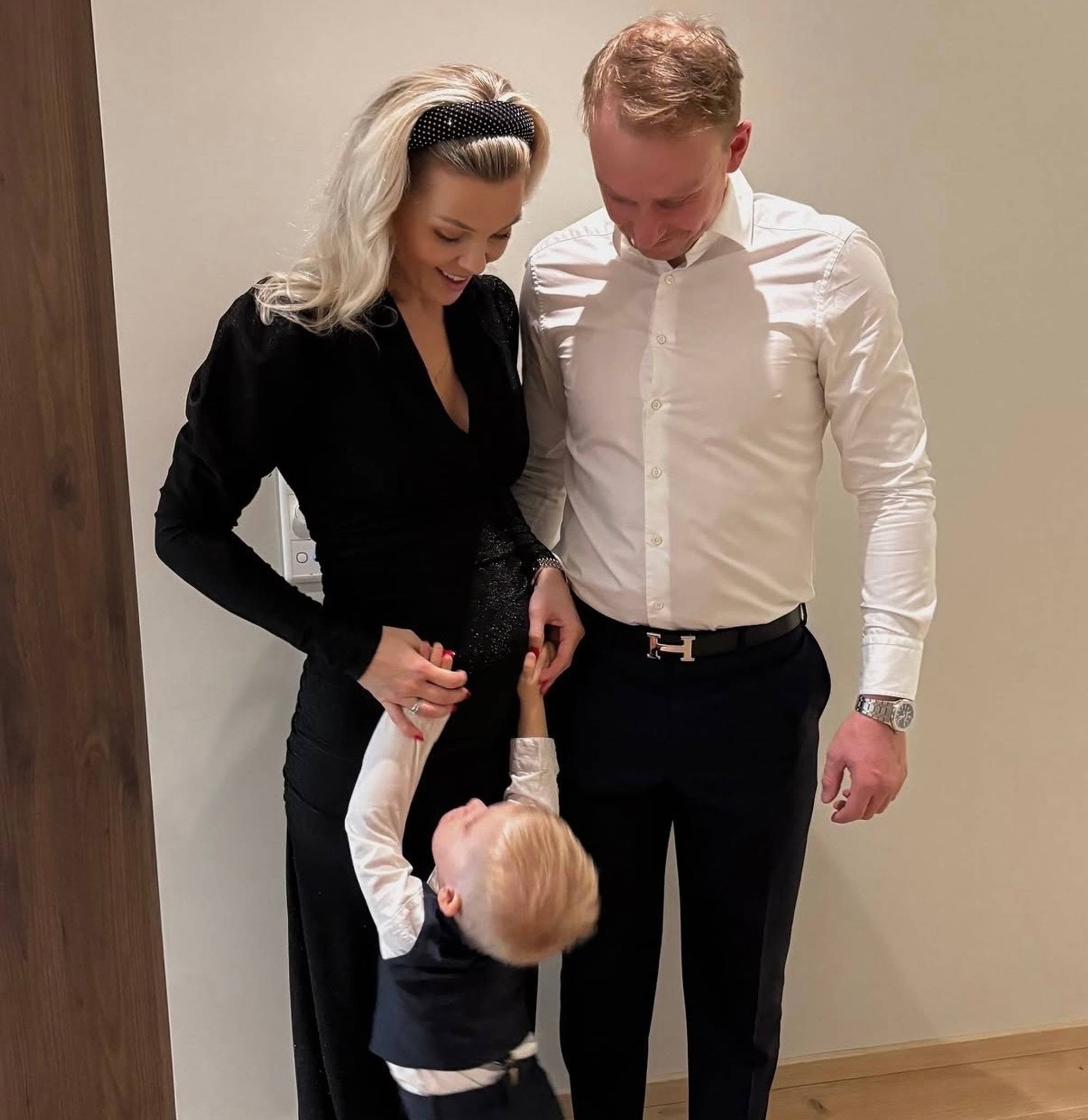 Gravid kvinne, mann og barn står sammen og holder hverandre på magen innendørs. (Bildebeskrivelsen er laget av en KI-tjeneste)