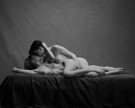 To nakne damer ligger bak hverandre på siden i senga mens de kysser