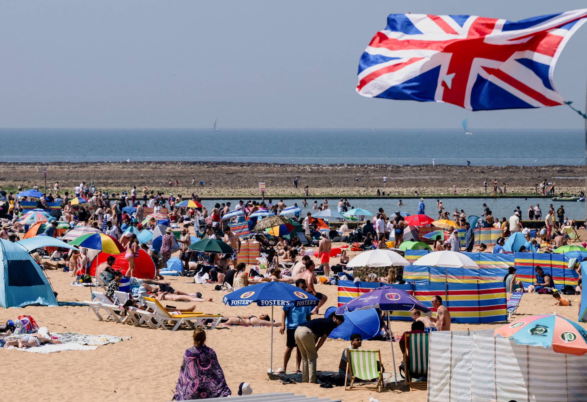 Strand med turister og et britisk flagg i forgrunnen