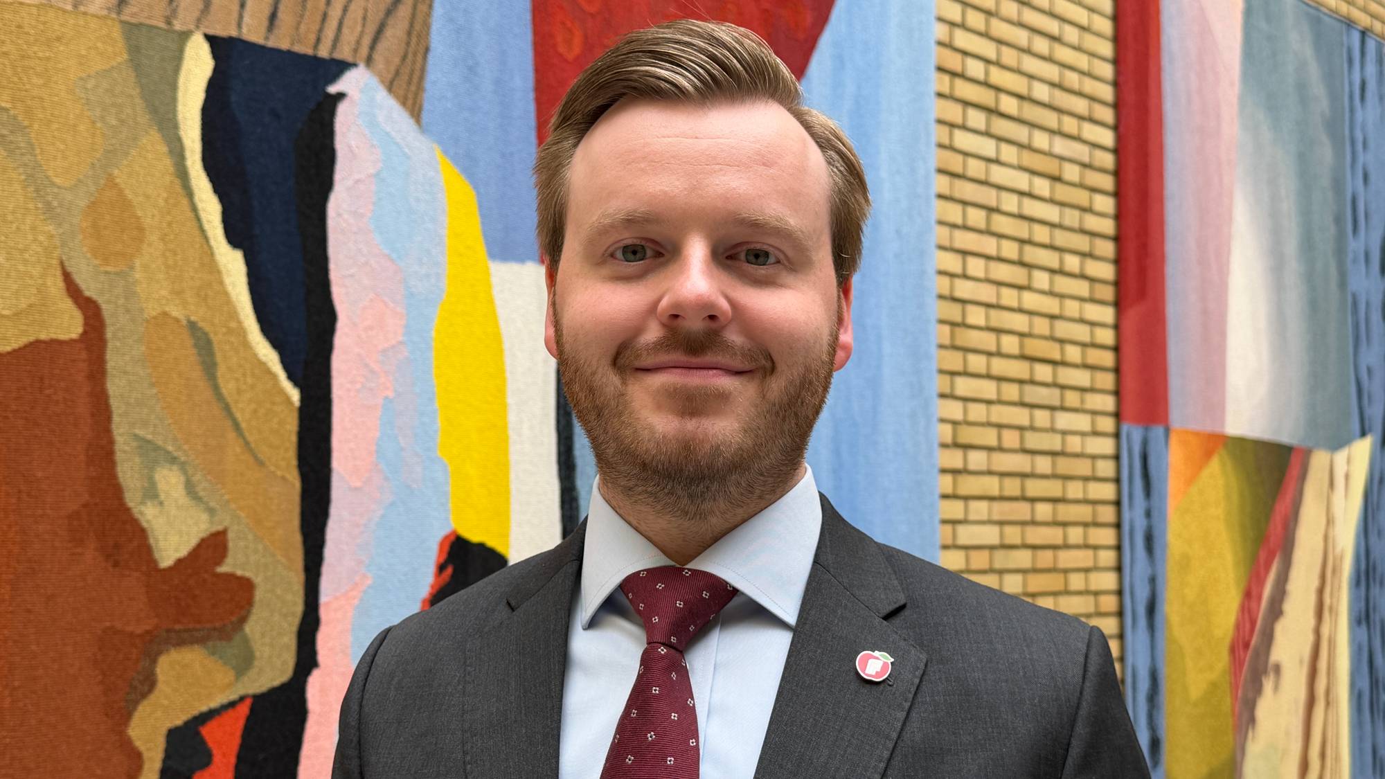 En mann i dress står foran en vegg og ser i kamera og smiler