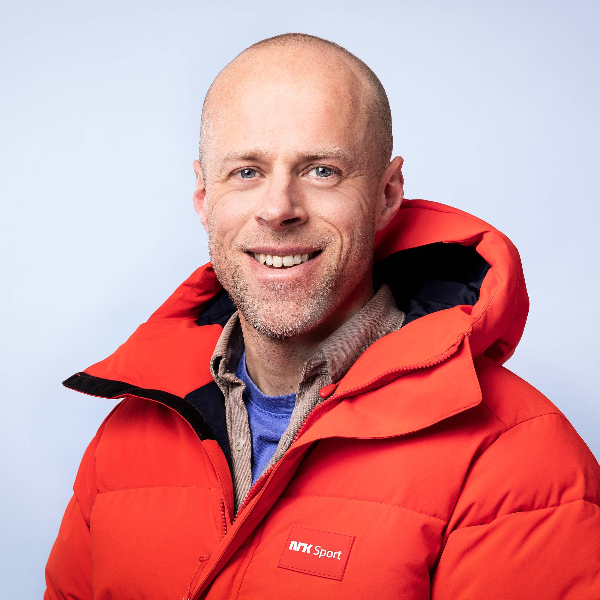 Portrett av en smilende mann i rød jakke med NRK Sport-logo foran en lys bakgrunn. (Bildebeskrivelsen er laget av en KI-tjeneste)