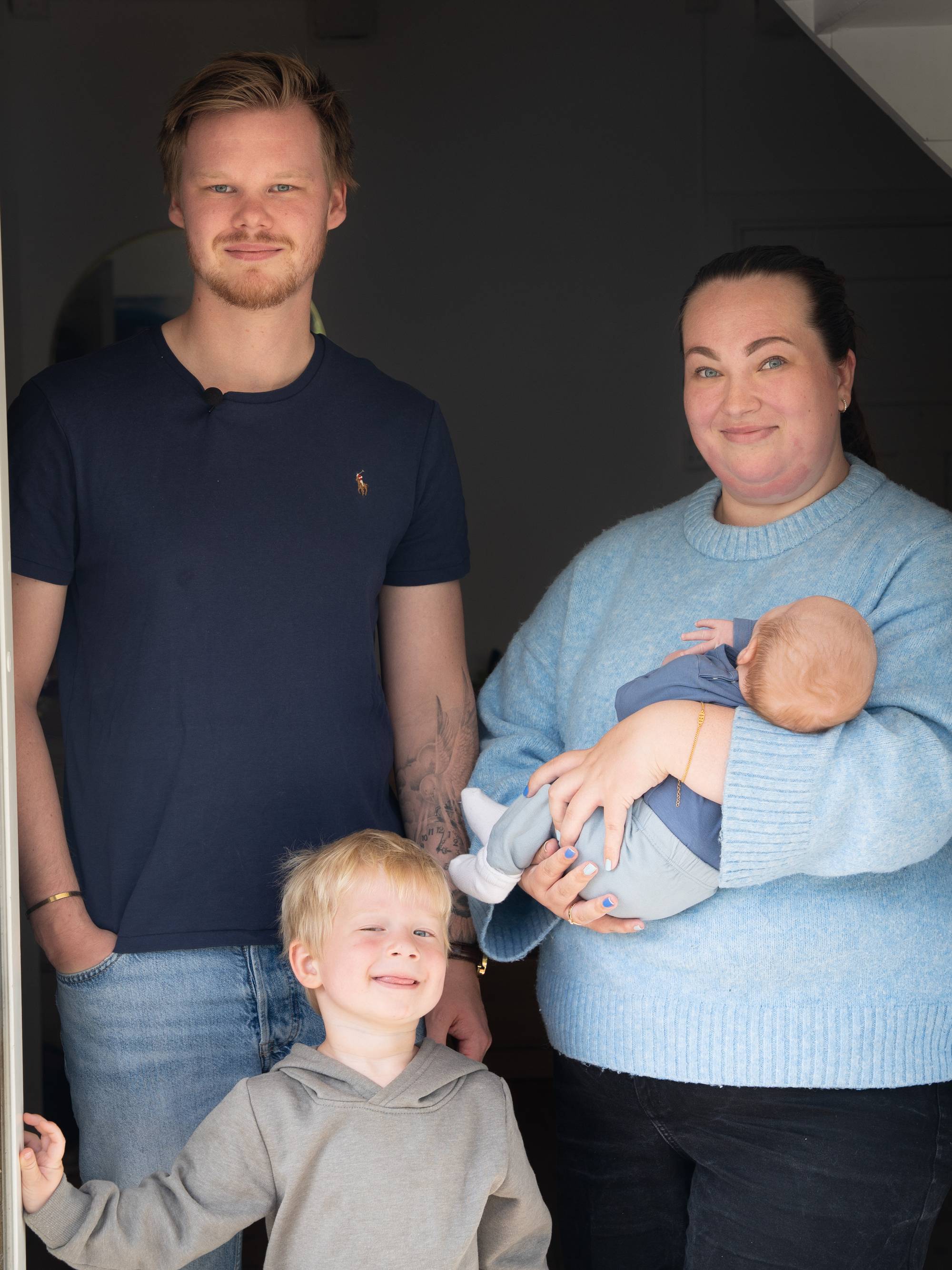 Småbarnsfamilie står i en døråpning. Foreldre med en baby og et eldre barn ser mot kameraet. (Bildebeskrivelsen er laget av en KI-tjeneste)