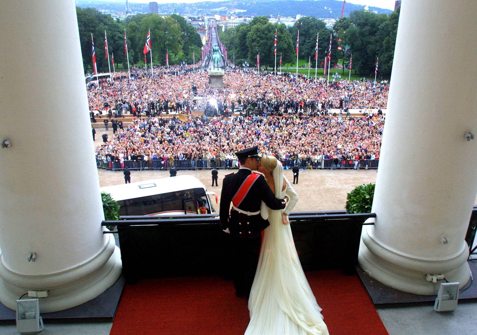 Kronprins Haakon Og Kronprinsesse Mette-Marit kysser hverandre på slottsbalkongen etter at de giftet seg 25. august 2001. Slottsplassen er full av folk.