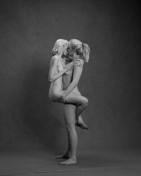En naken kvinne står på gulvet og løfter en annen naken kvinne mens de kysser