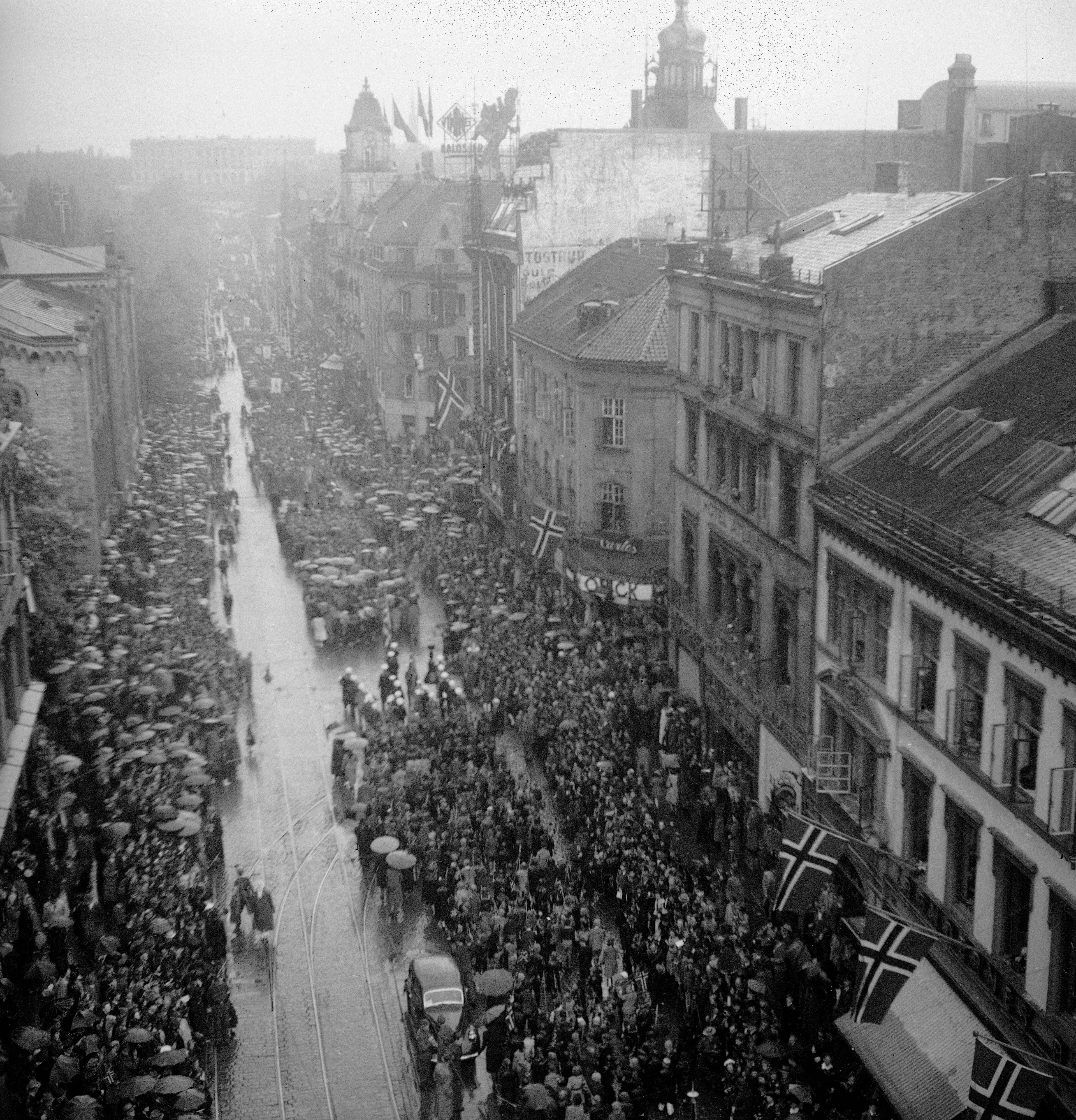 17.mai -feiring Oslo 1945. Regn la ingen demper på festlighetene under den første feiringen av nasjonaldagen etter krigen. Her folkemassen som deltok i festmøtet på Rådhusplassen. Vestbanen i bakgrunnen.